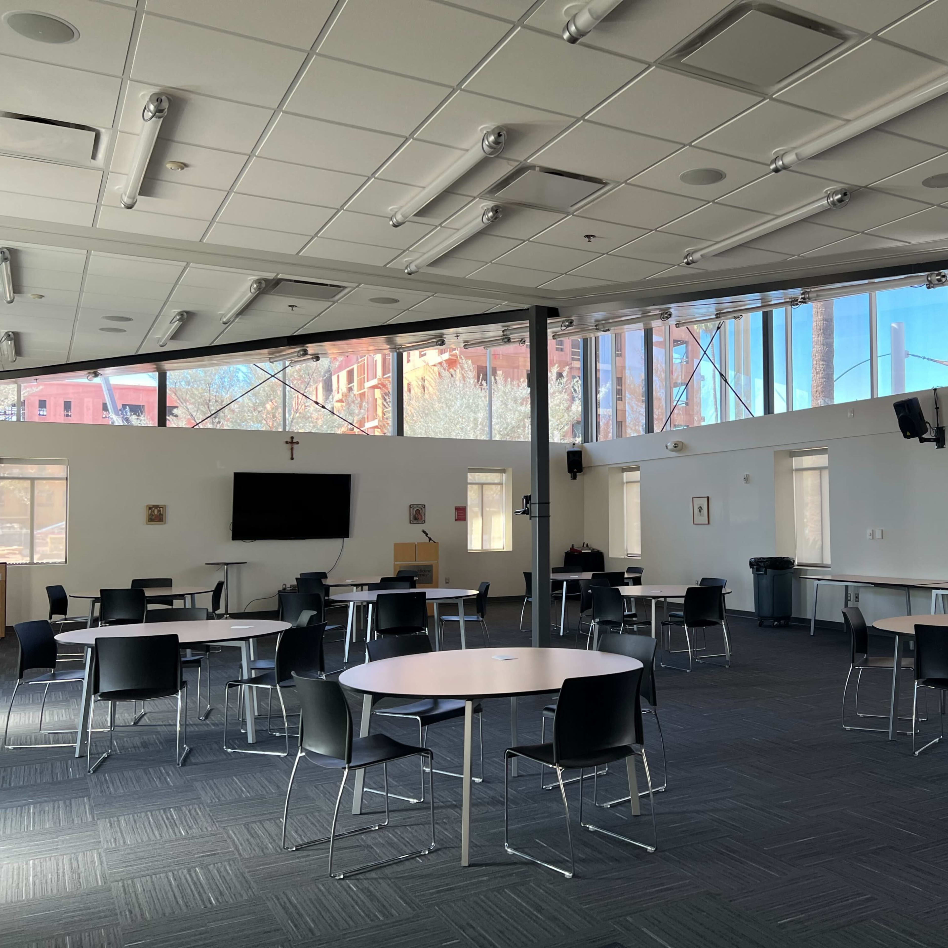 A spacious, well-lit room with several round tables and chairs arranged for meetings, featuring large windows that overlook a construction site.