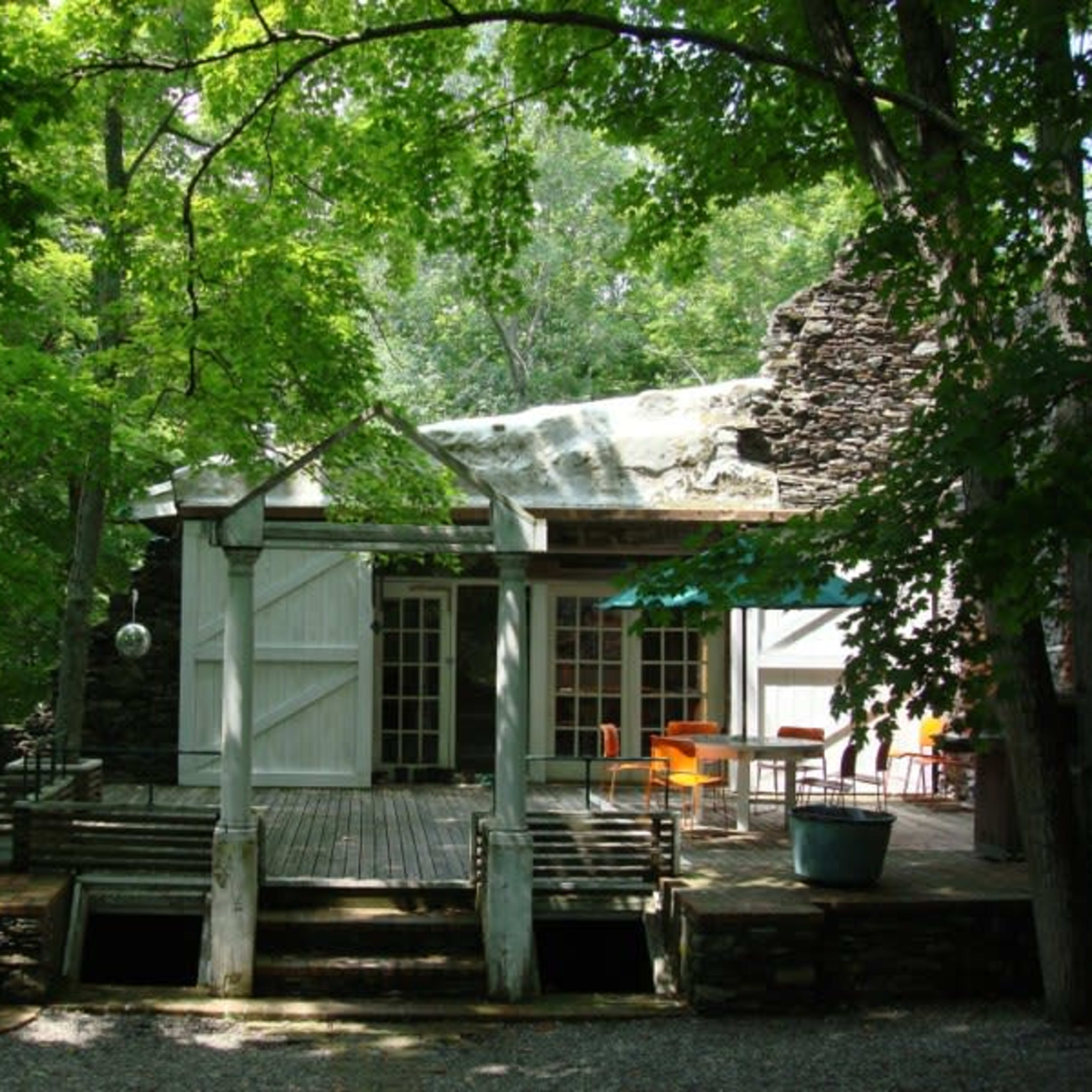 A modern cabin is situated in a wooded area, featuring large glass doors that open onto a wooden deck surrounded by trees.