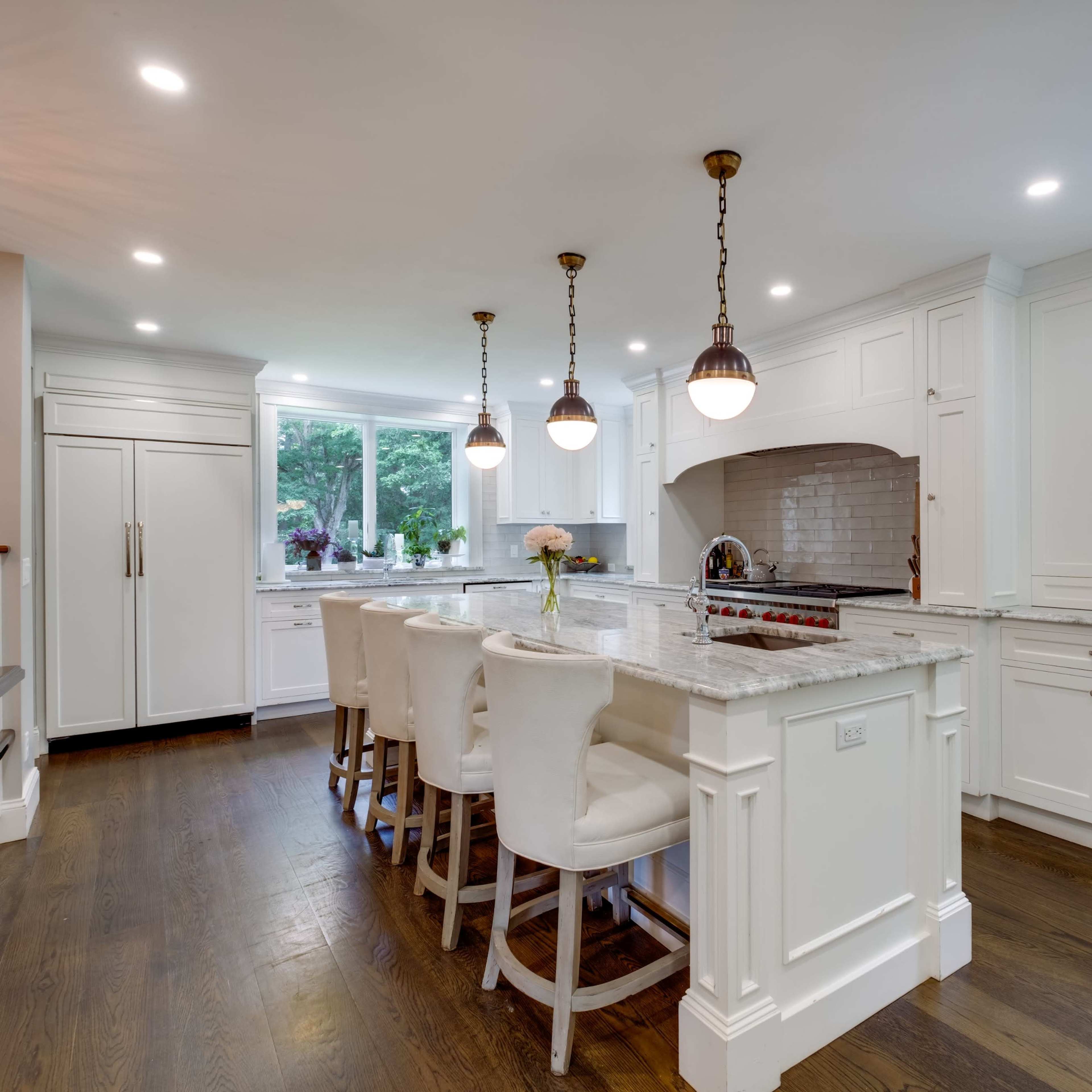 A modern kitchen features white cabinetry, a large island with seating, and pendant lighting above.