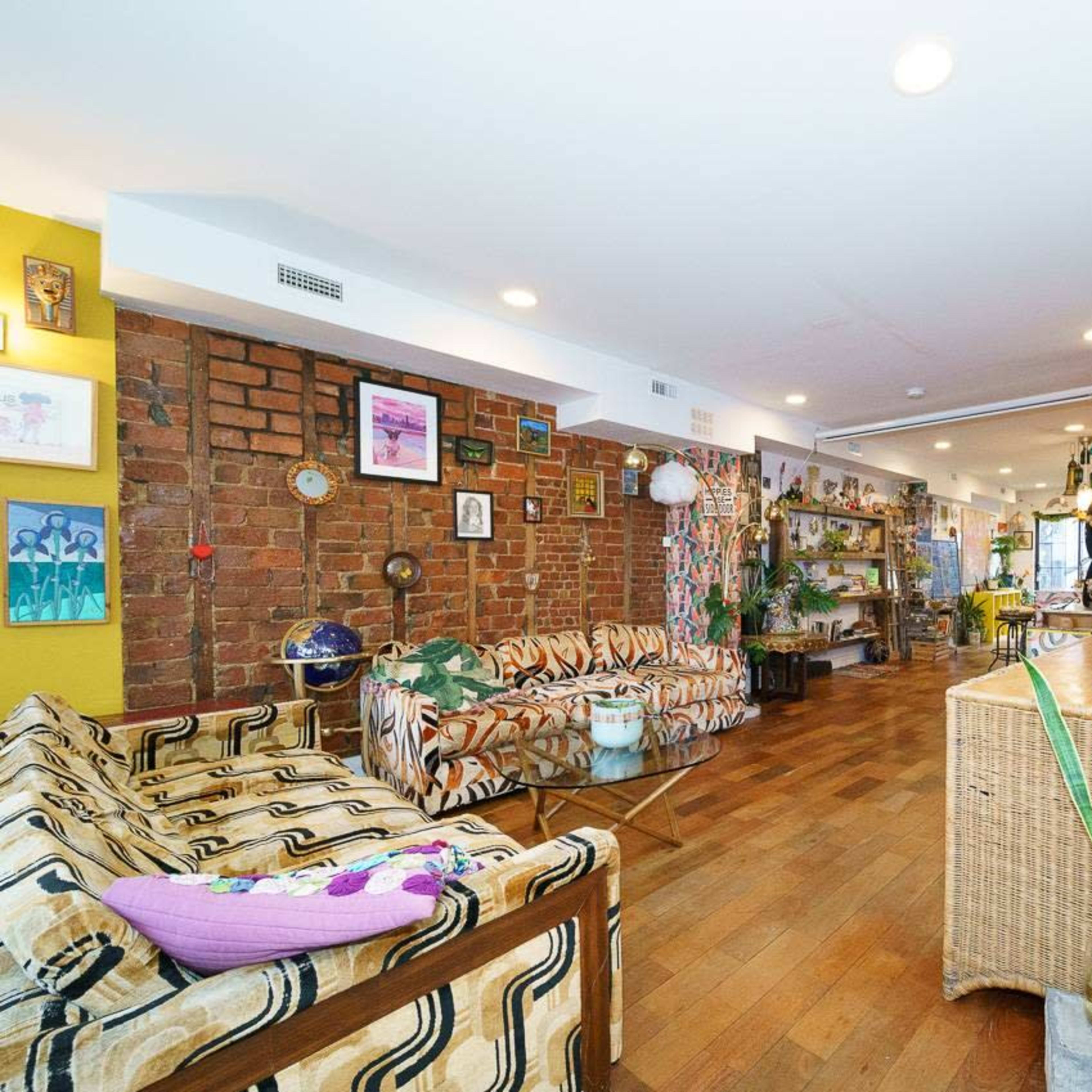 A spacious living area features patterned sofas, exposed brick walls, and wooden floors, with a staircase leading to an upper level.
