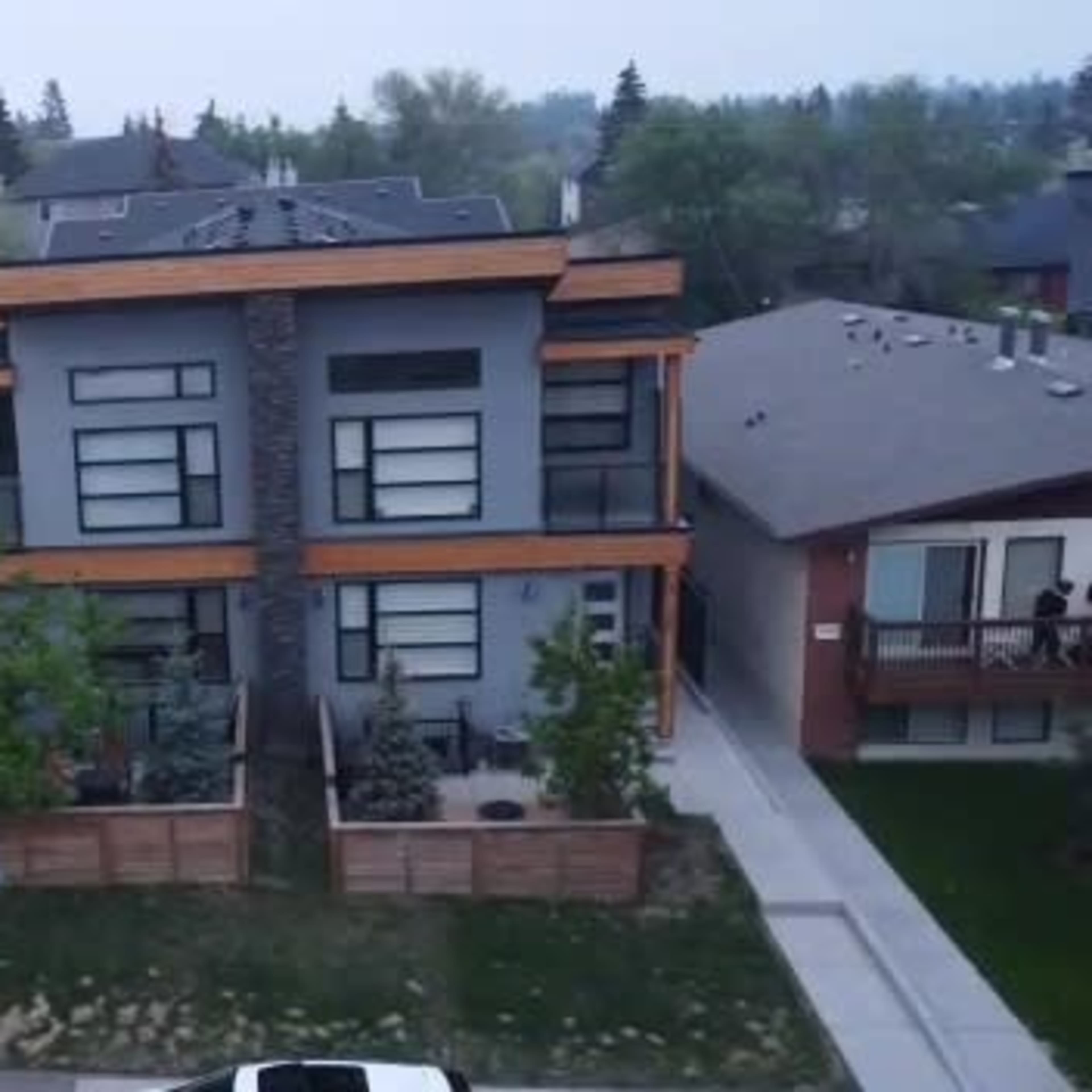 A row of modern multi-family homes with a mix of dark and light-colored facades, separated by sidewalks and small yards.