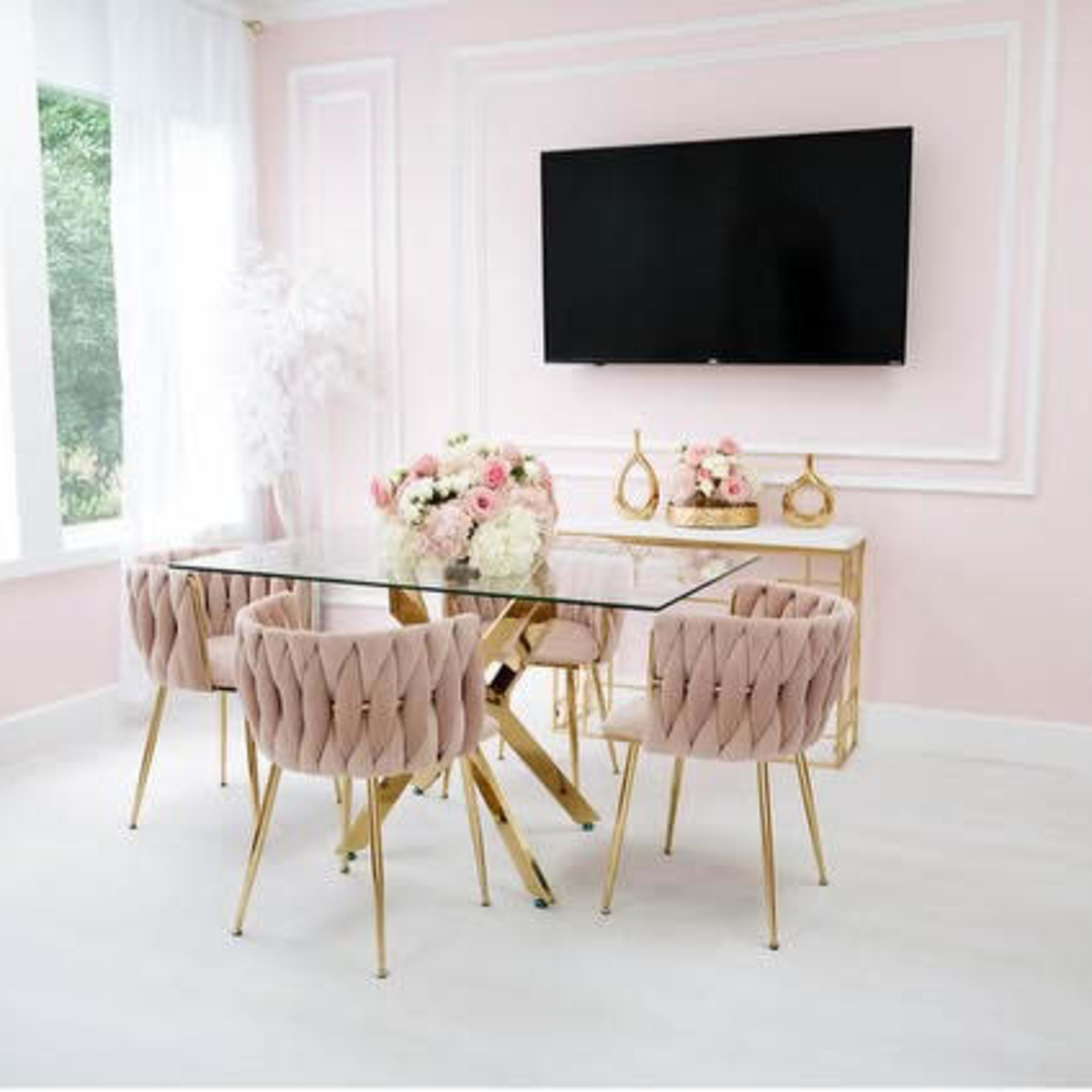 A modern dining area with a glass table surrounded by pink upholstered chairs and a large wall-mounted TV in a softly lit room with pink walls.