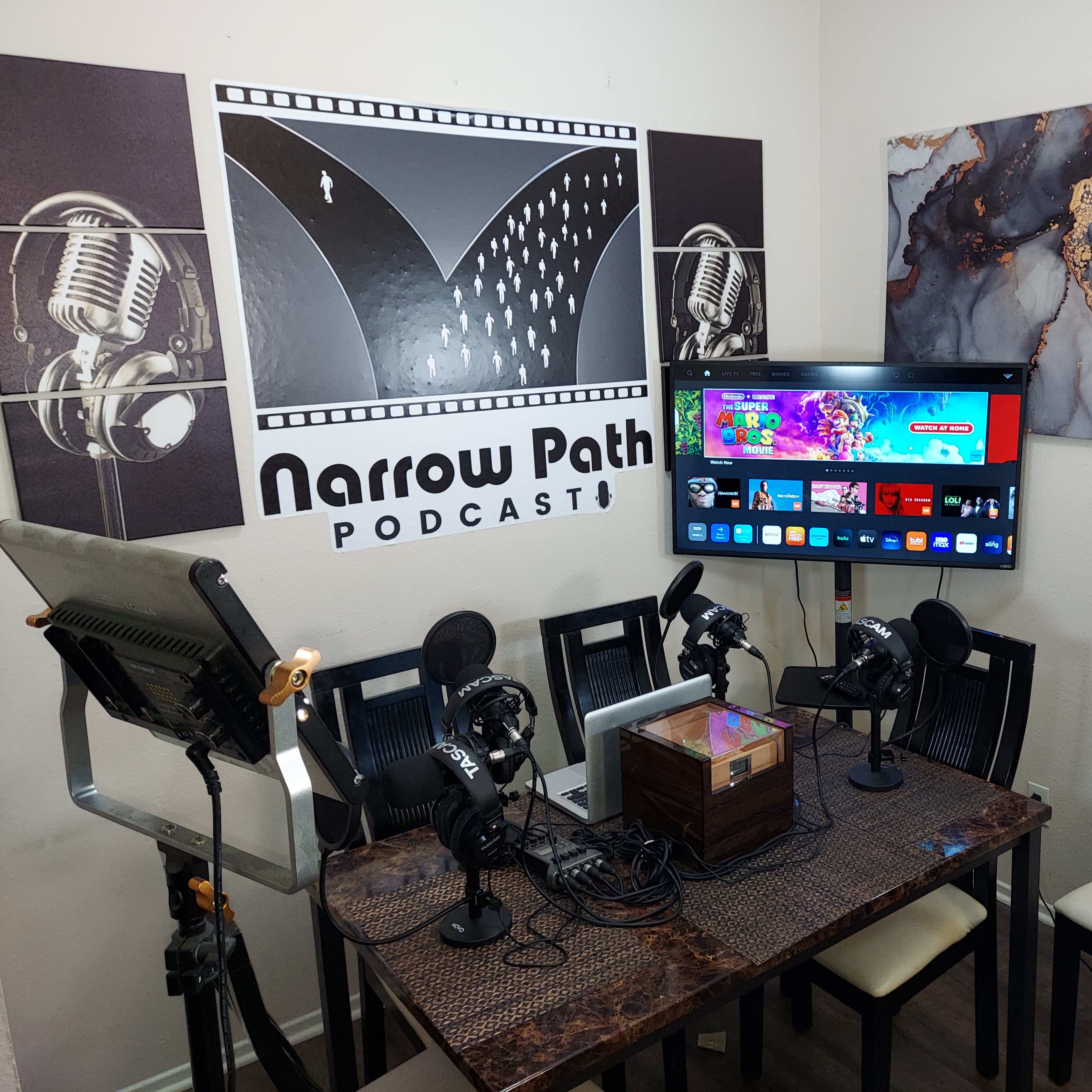 A podcasting setup featuring a table with microphones, a television displaying content, and a backdrop with the text "Narrow Path PODCAST."