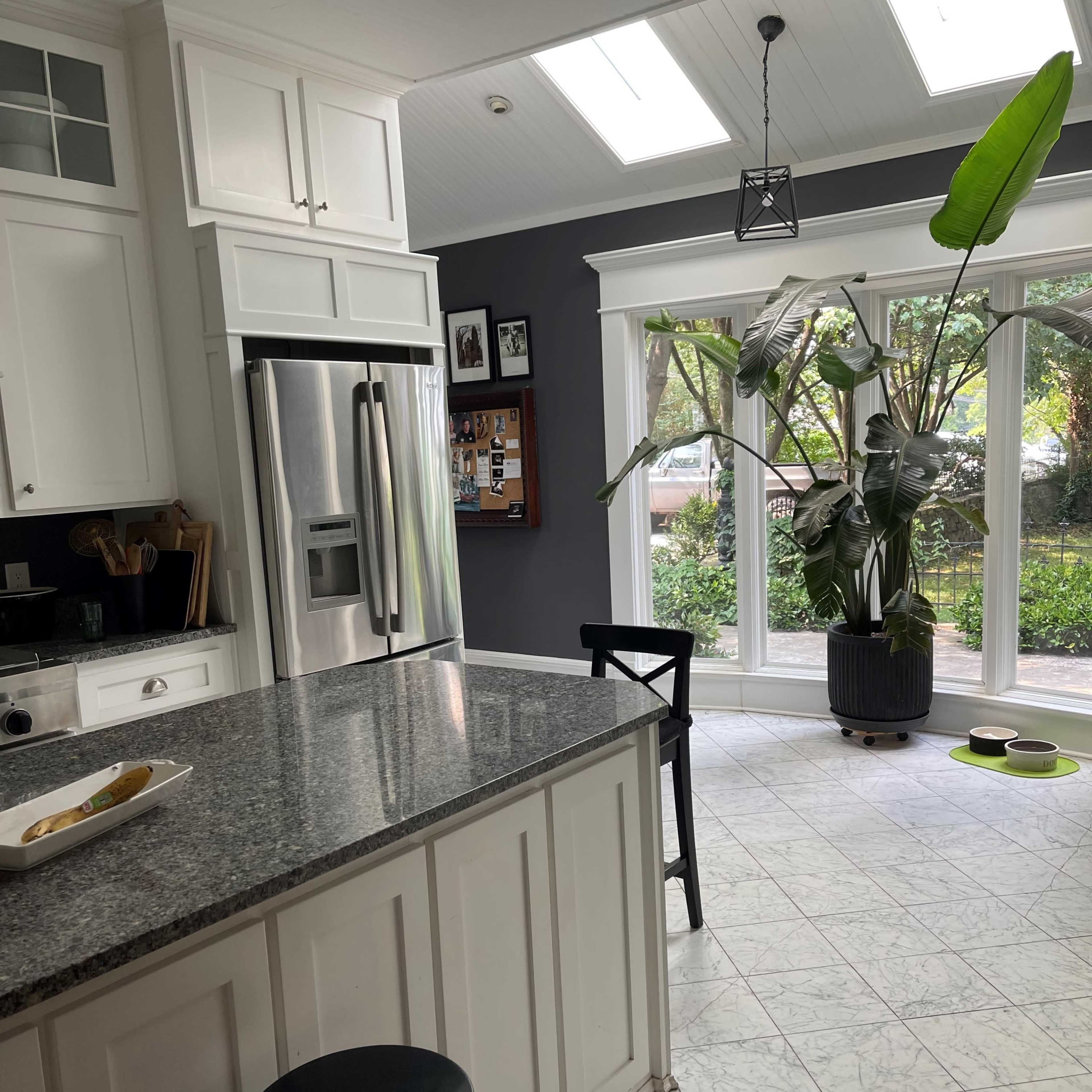 A bright kitchen features granite countertops, stainless steel appliances, and a large window with a potted plant.