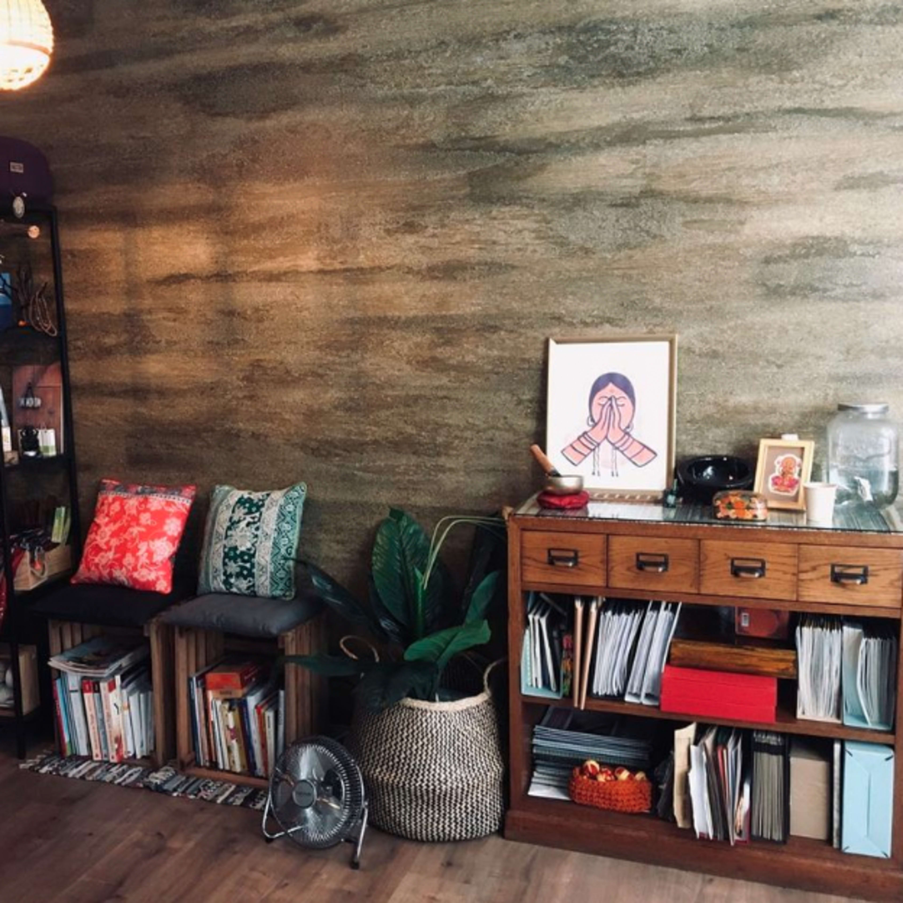 A cozy interior with a bookshelf, a potted plant, and a framed artwork against a textured wall.