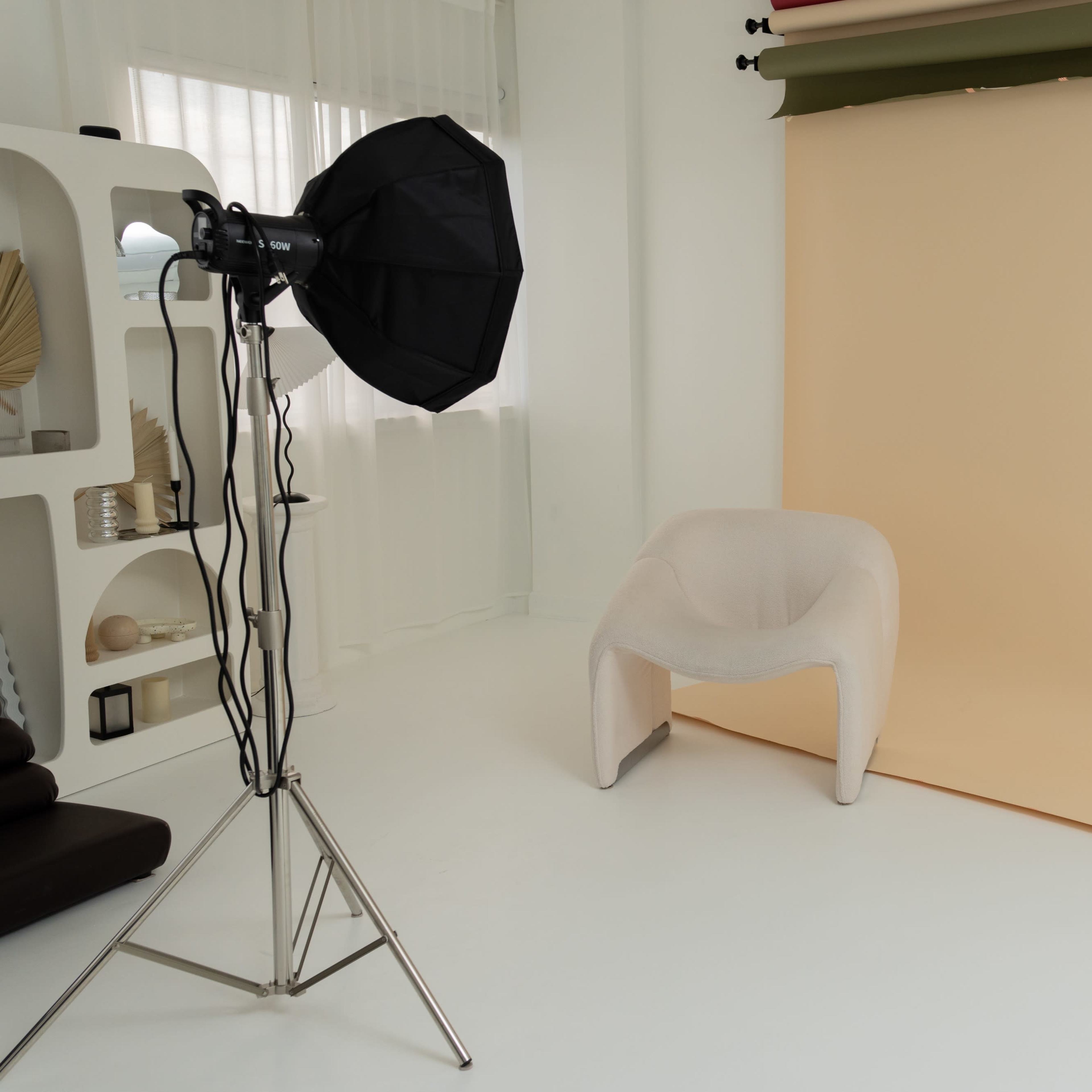 A minimalist photography studio setup with a light source, a neutral background, a modern chair, and a side table.