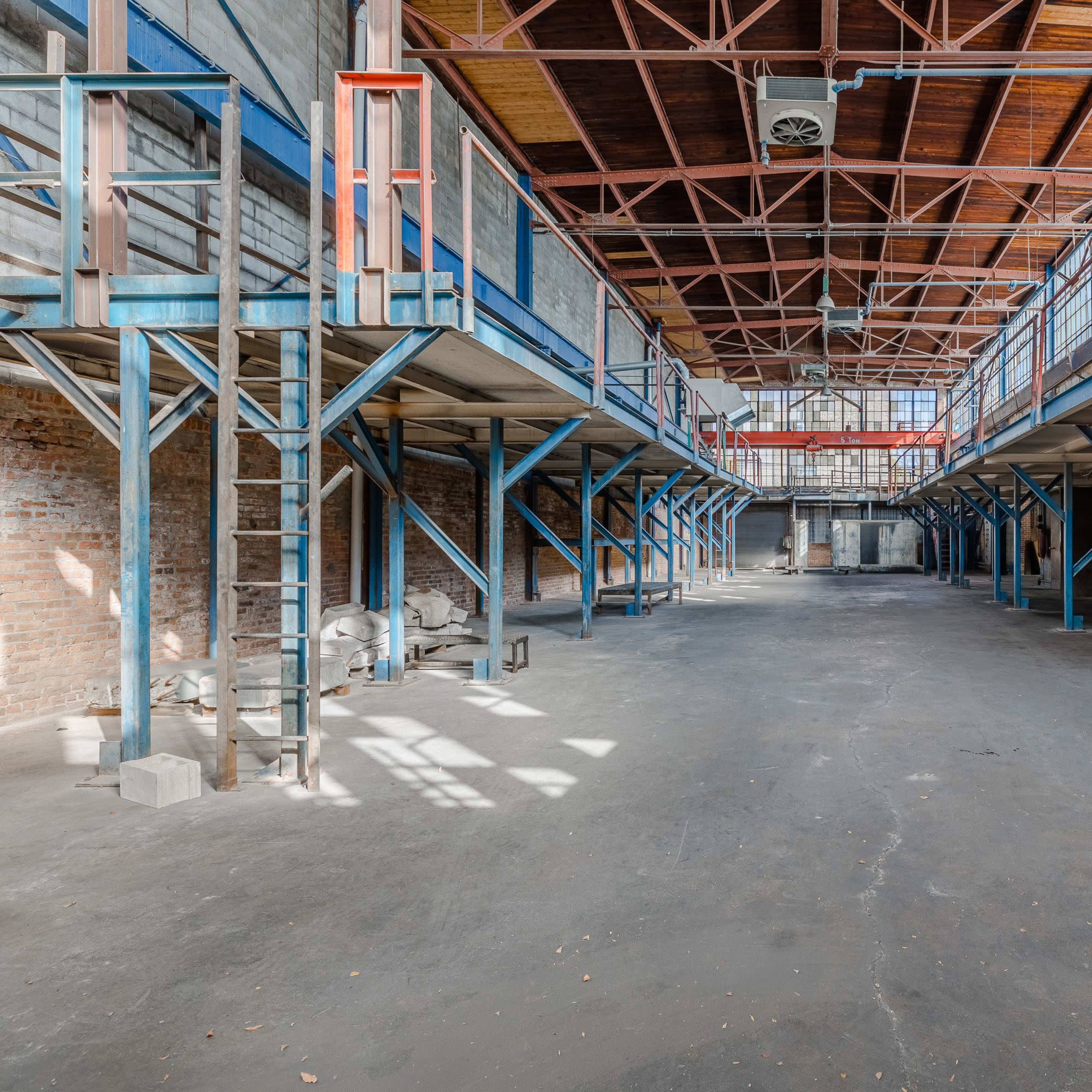 An expansive, empty industrial warehouse with multiple levels, concrete floors, and exposed metal beams.