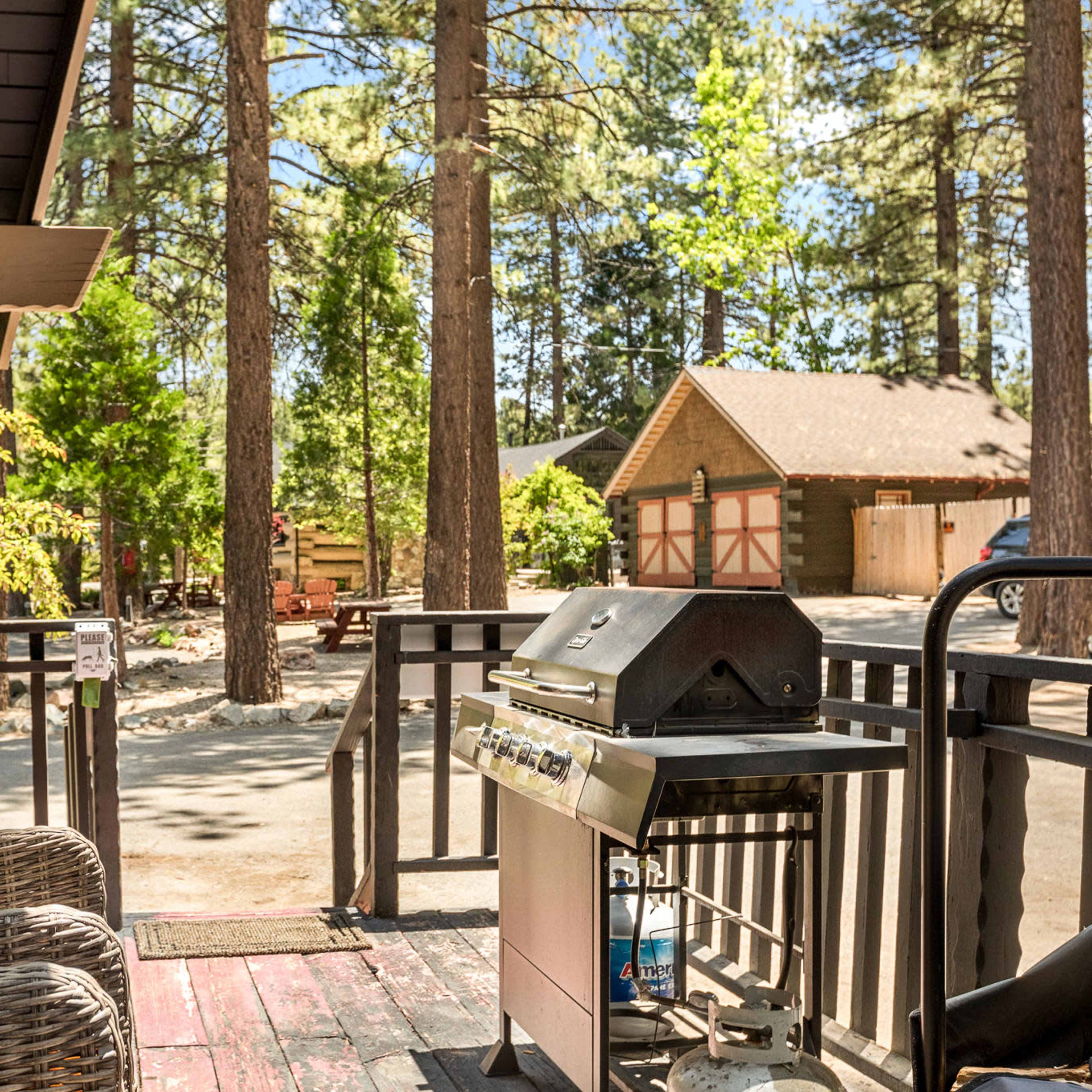 A porch with two chairs and a grill overlooks a wooded area and a nearby garage.