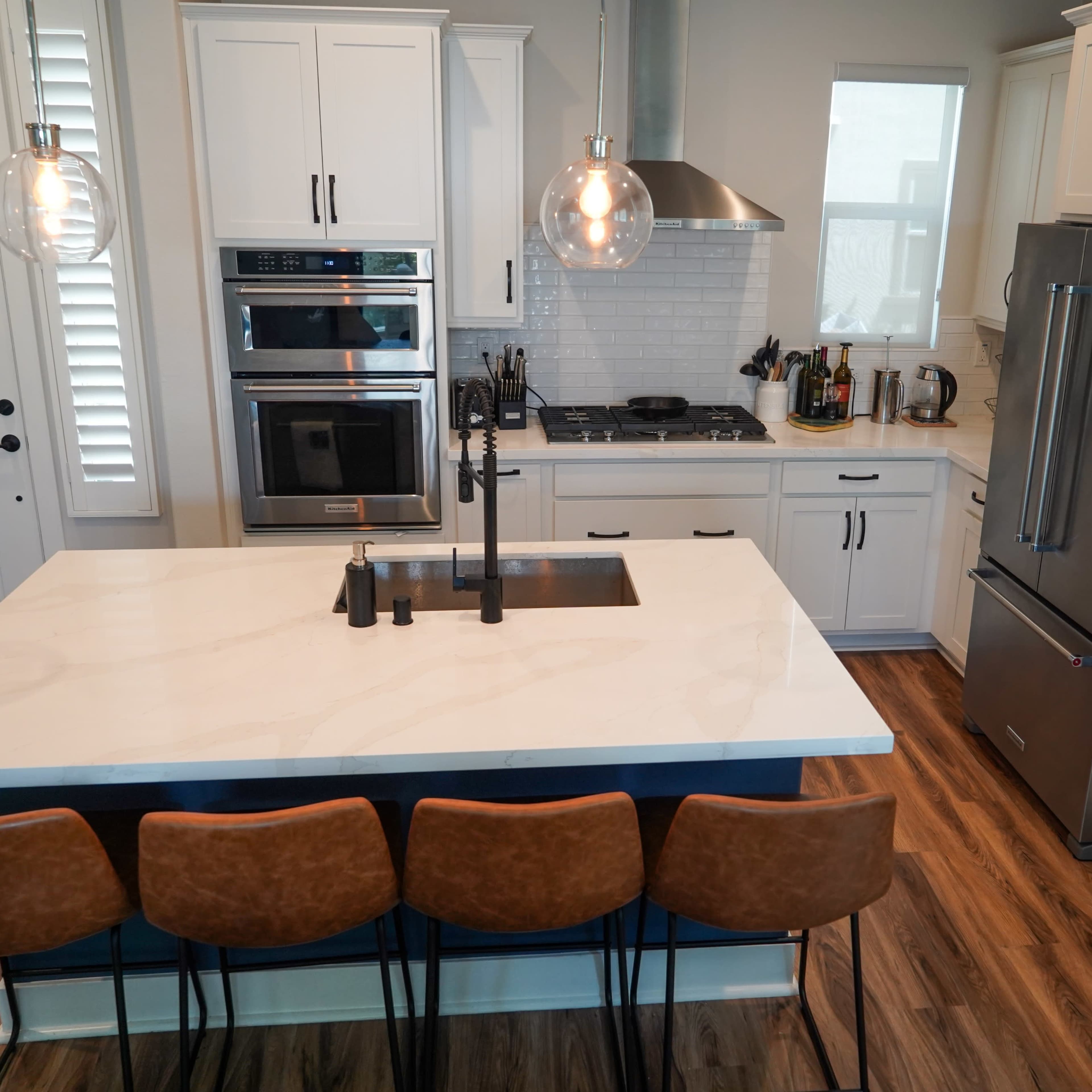 A modern kitchen featuring white cabinets, a large island with a sink, and four brown barstools.