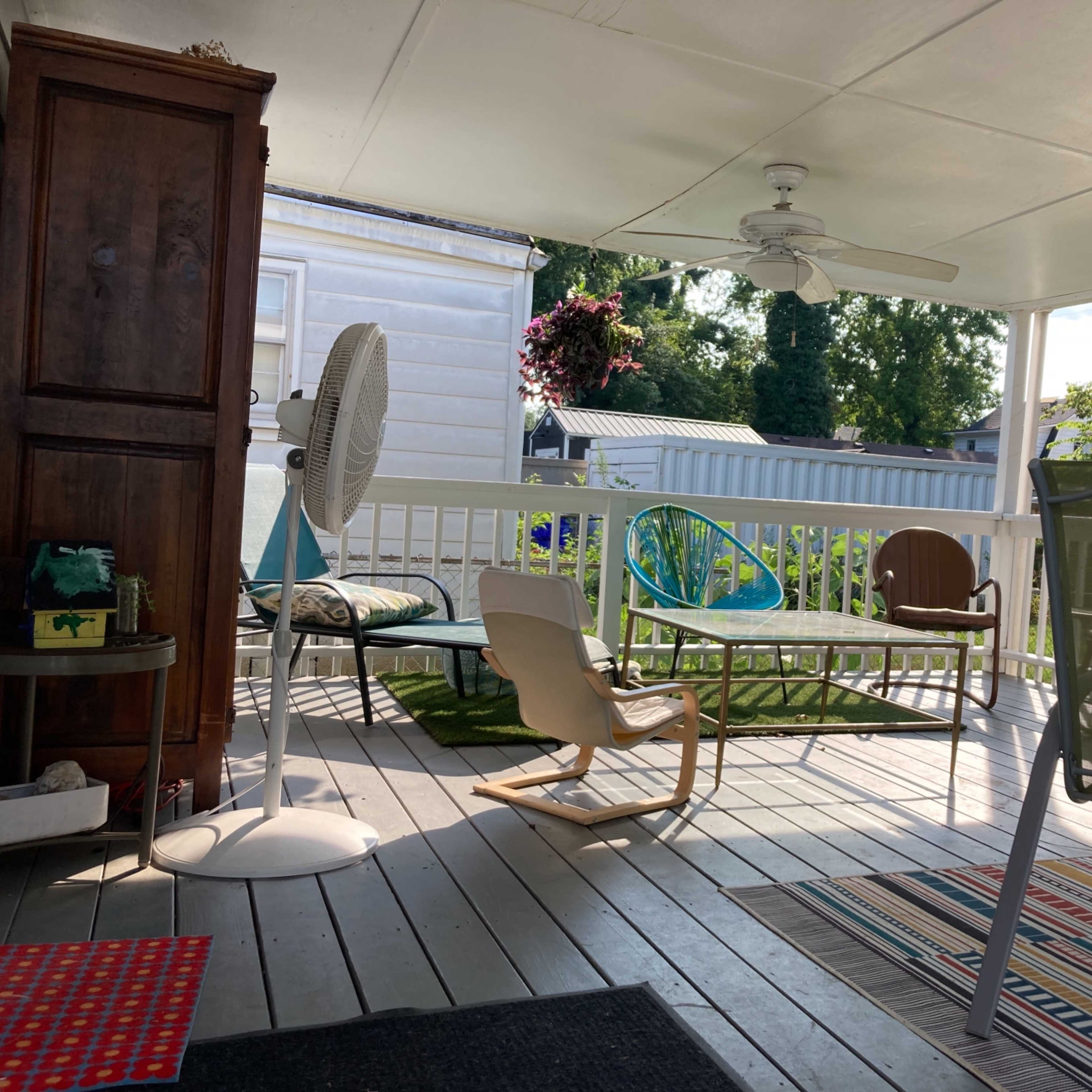 A covered porch features various seating options, a ceiling fan, and potted plants.