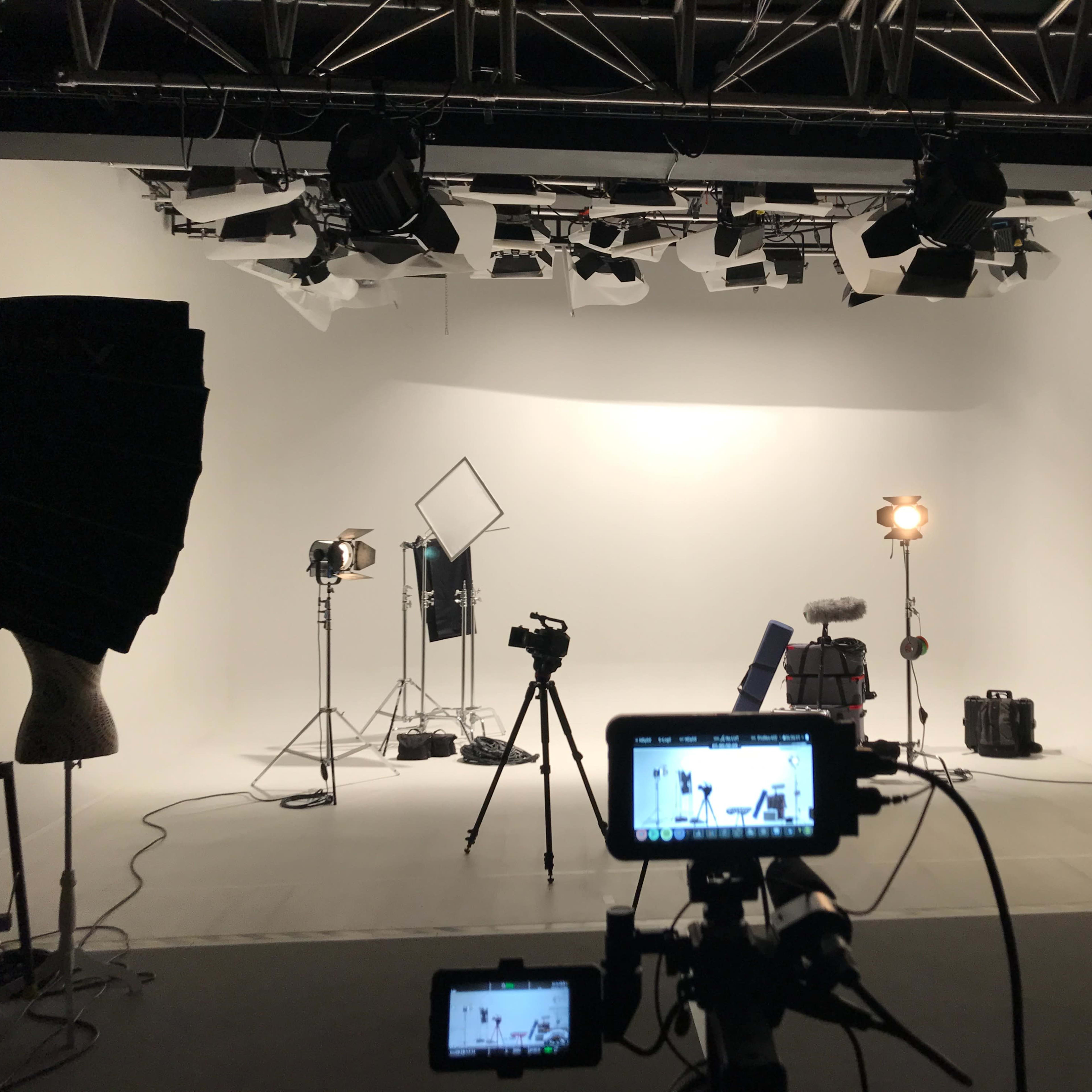 A well-equipped photography studio with various lights, cameras, and equipment set up against a white backdrop.