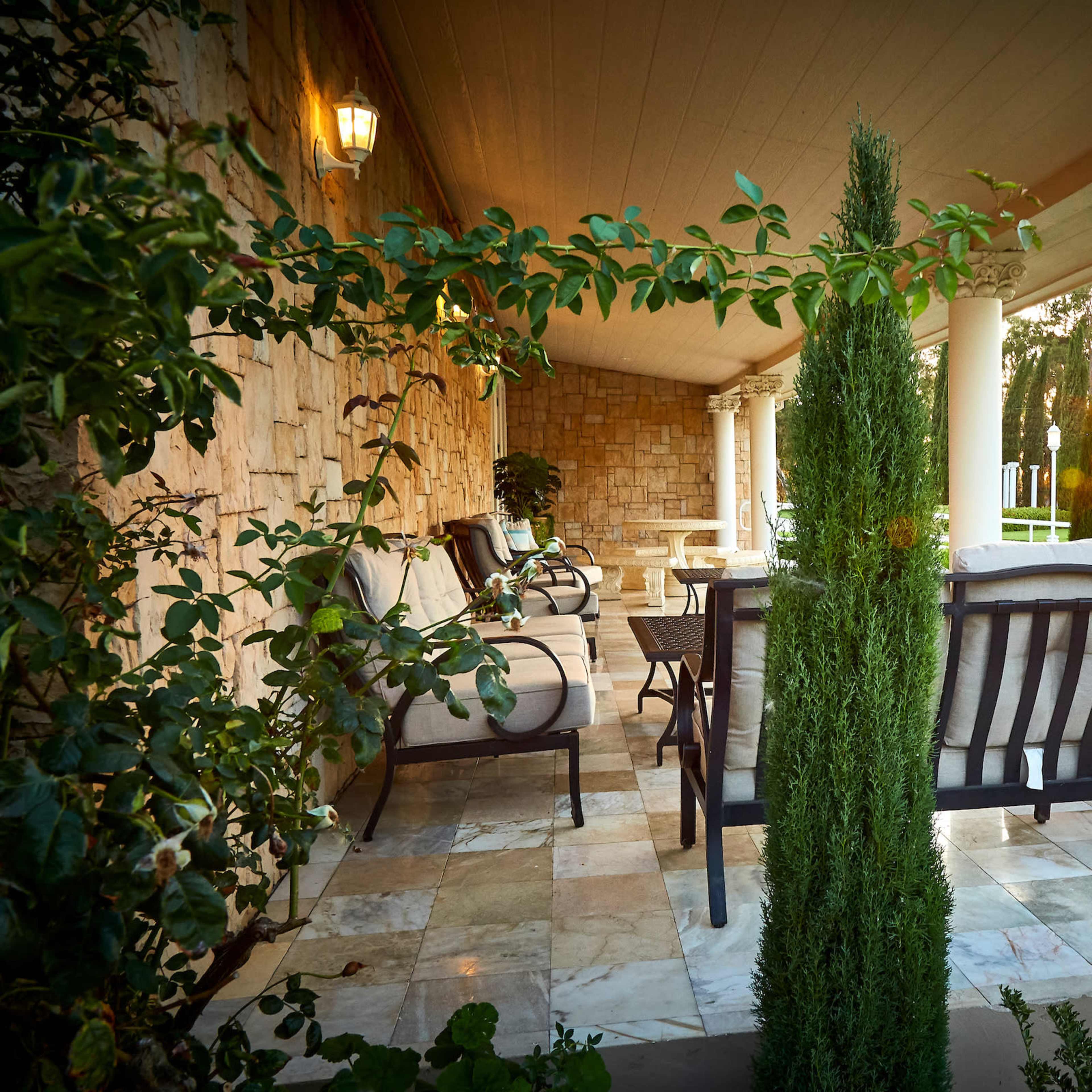 A covered patio features wooden furniture and vertical shrubs, with a sunset illuminating the outdoor area.