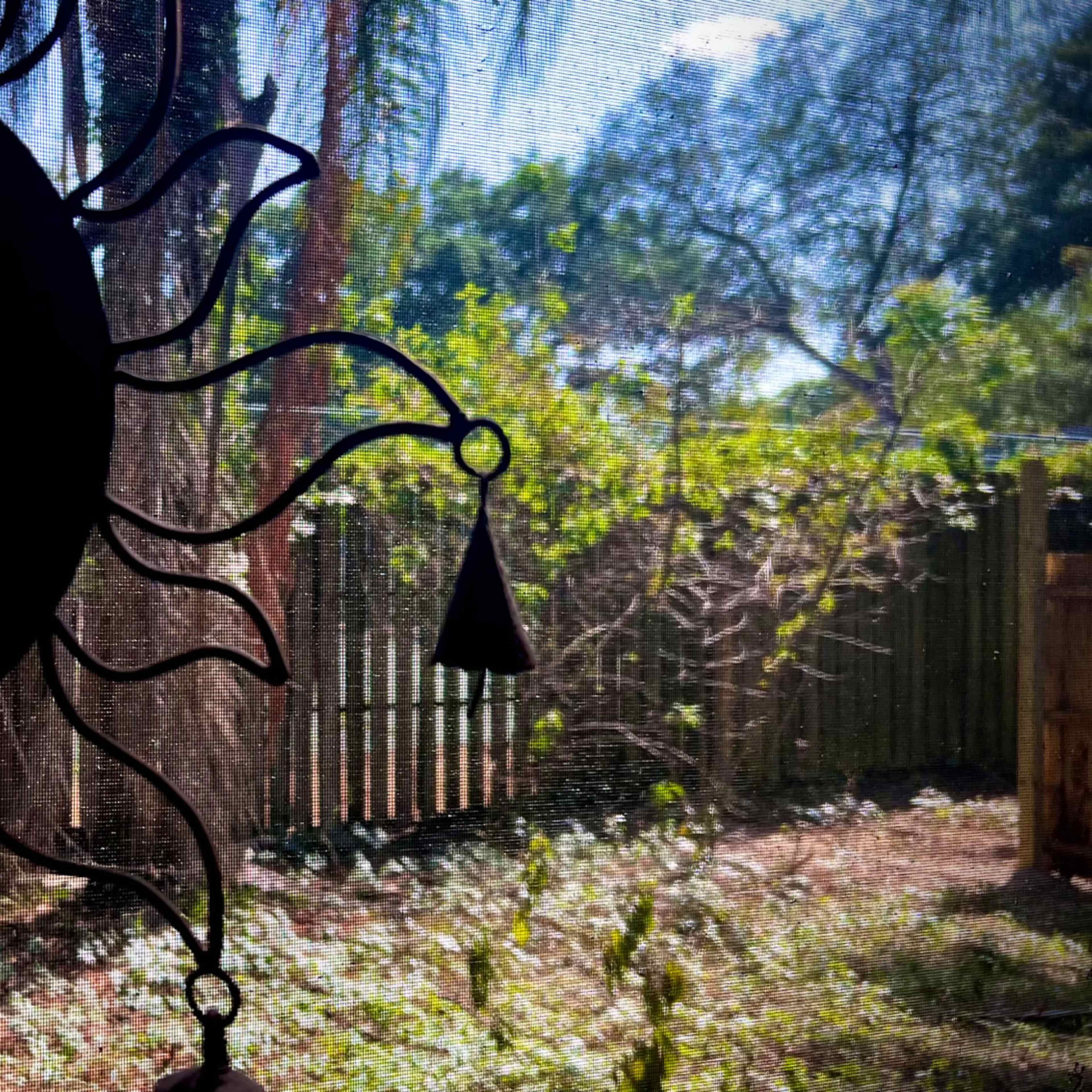 A decorative sun sculpture hangs in front of a window, overlooking a grassy backyard surrounded by trees.