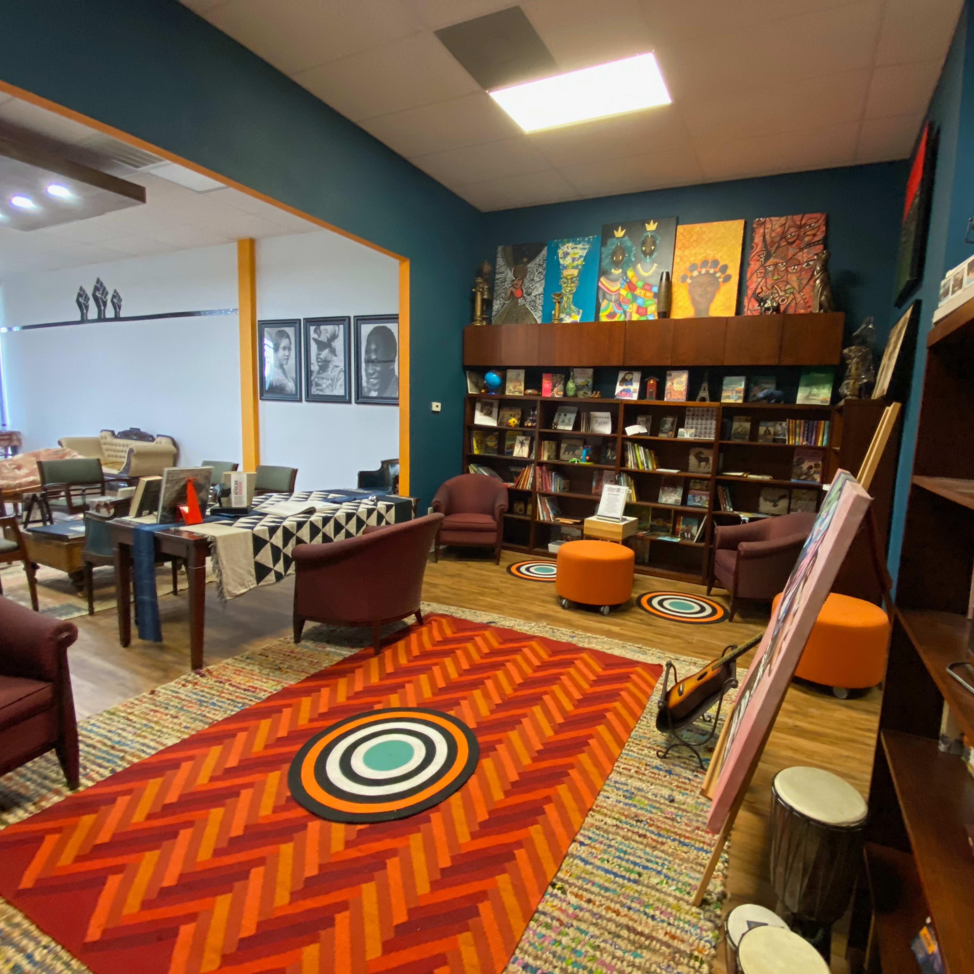 A cozy room with colorful art on the walls, bookshelves filled with books, and comfortable seating arranged around a patterned rug.