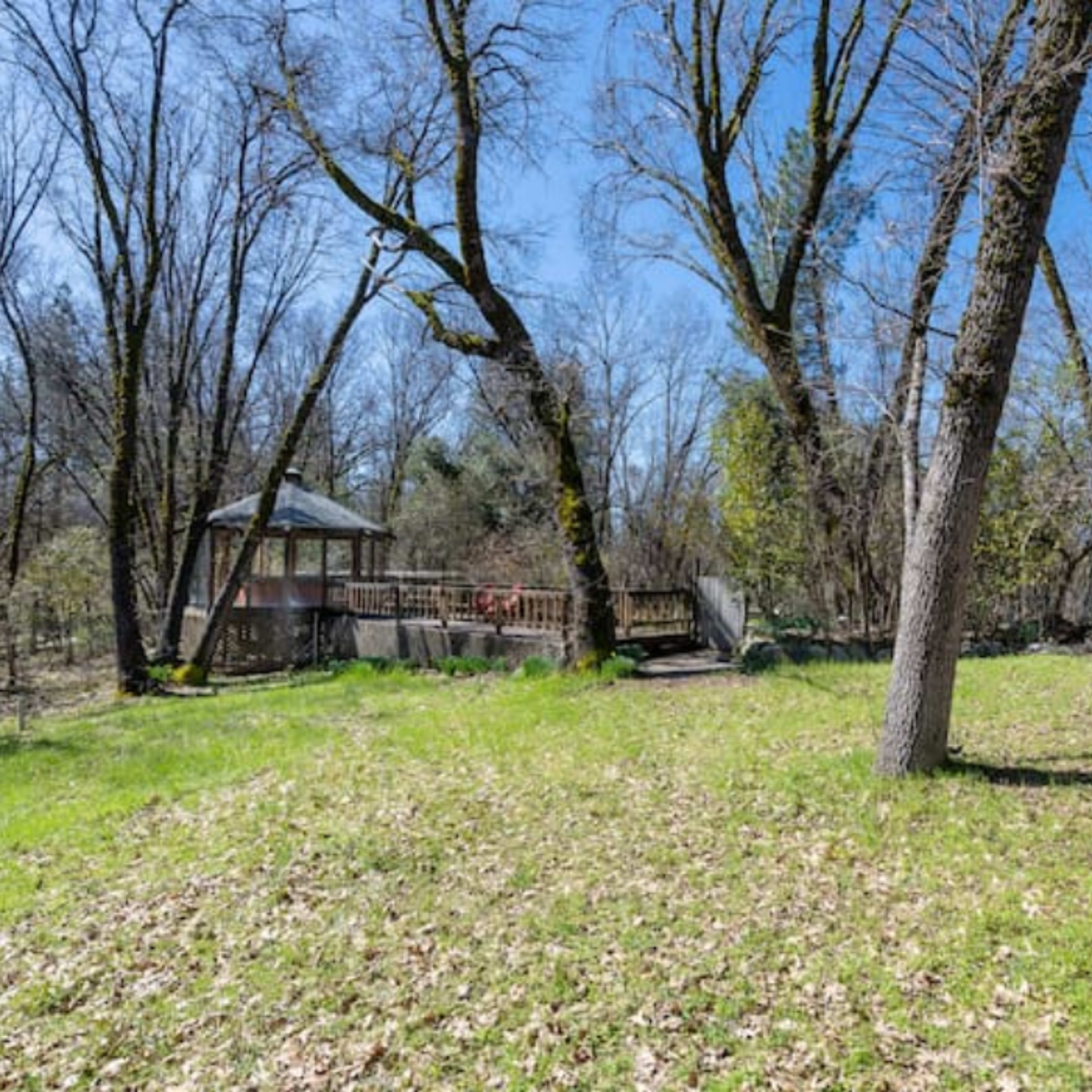 A grassy area with scattered trees and a gazebo is visible beside a wooden deck and a glass-enclosed structure.