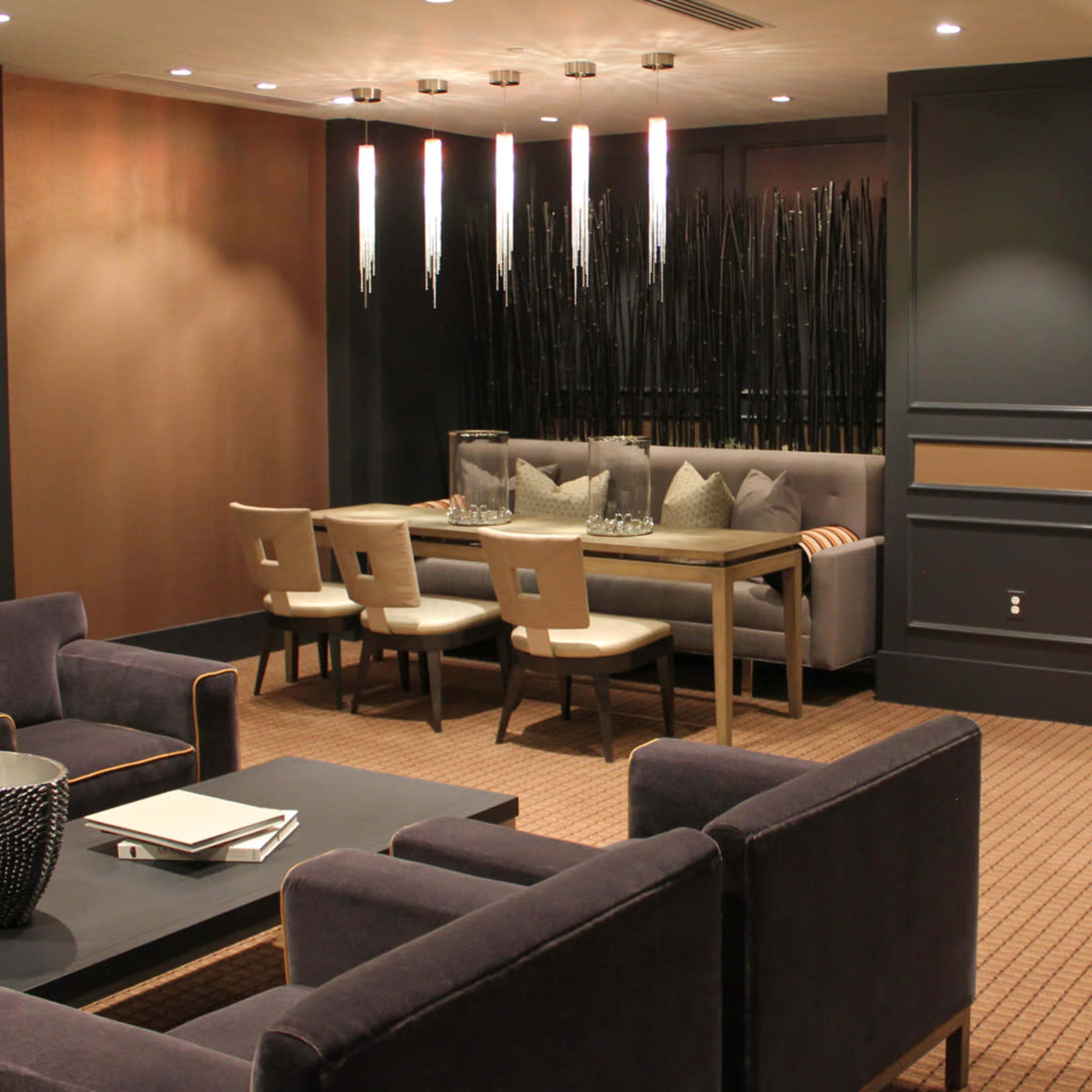 A modern lounge area featuring seating arrangements, a dining table, decorative lighting, and a television mounted on the wall.