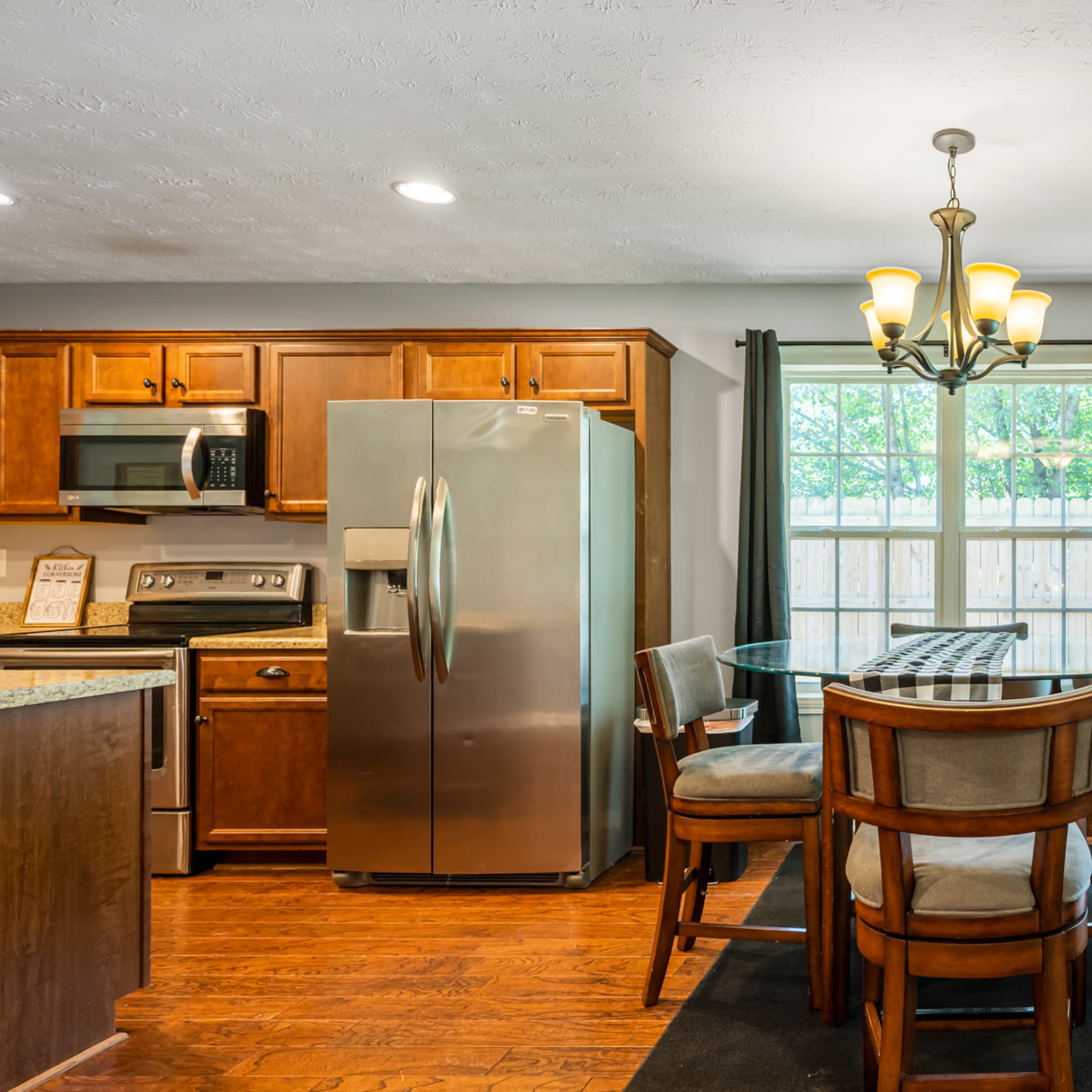 A kitchen features wooden cabinets, a stainless steel refrigerator, and a glass-topped dining table with four chairs.