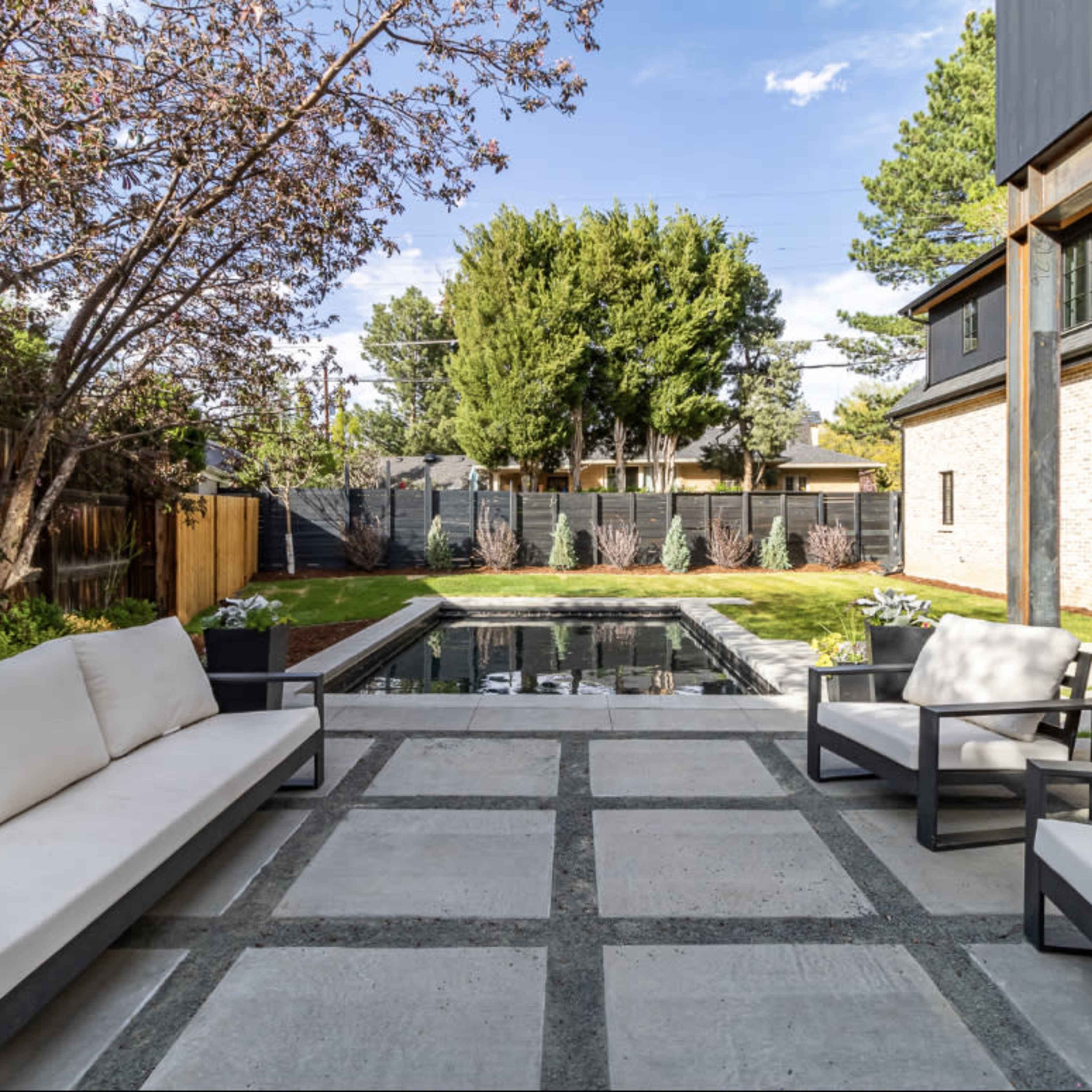 A modern backyard patio with stone tiles, outdoor seating, and a pool surrounded by landscaped greenery.