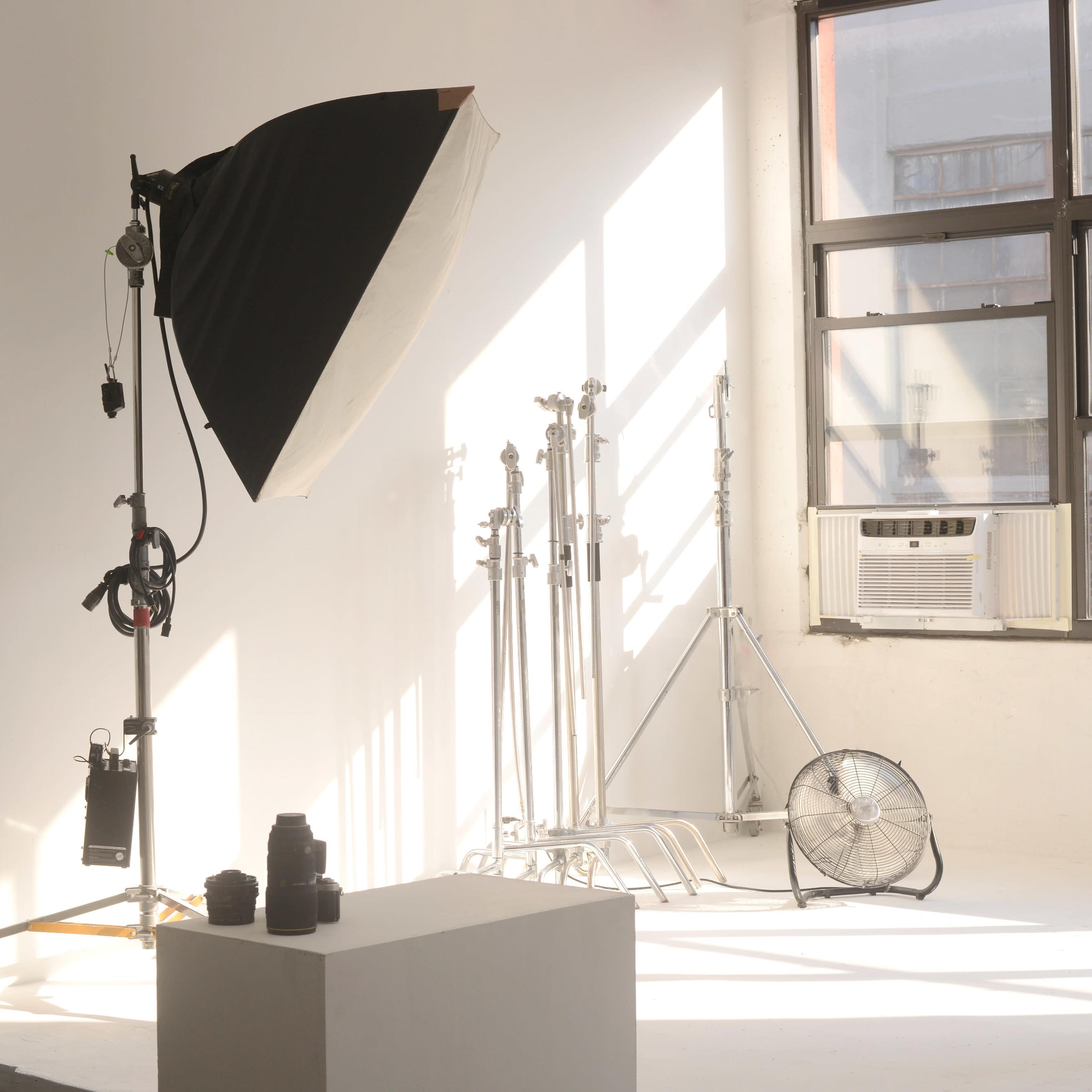 A photography studio with a large softbox light, several light stands, a fan, and a camera placed on a pedestal in a brightly lit space.