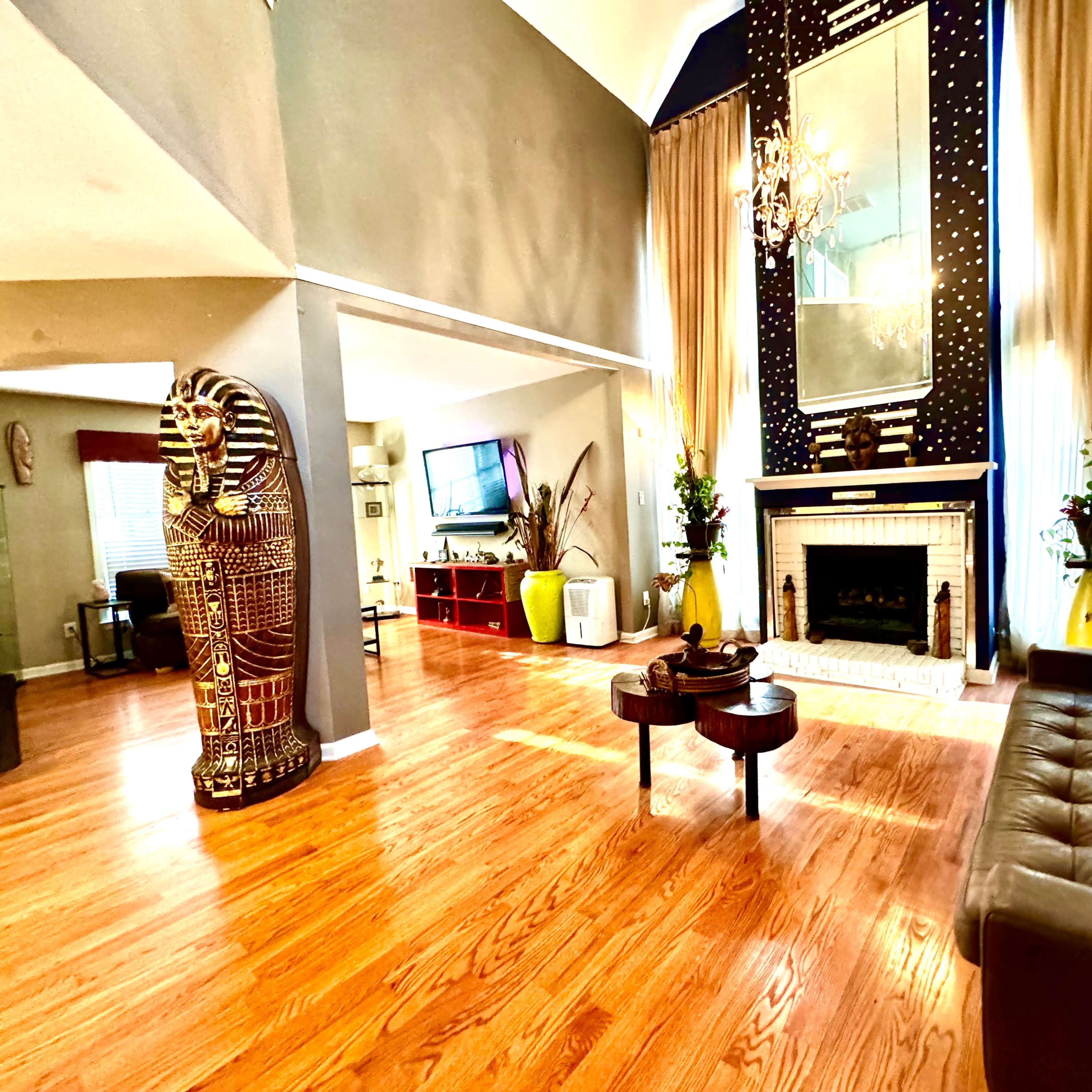 A spacious living room featuring hardwood floors, a large mirror, a decorative fireplace, and a golden Egyptian-style statue.