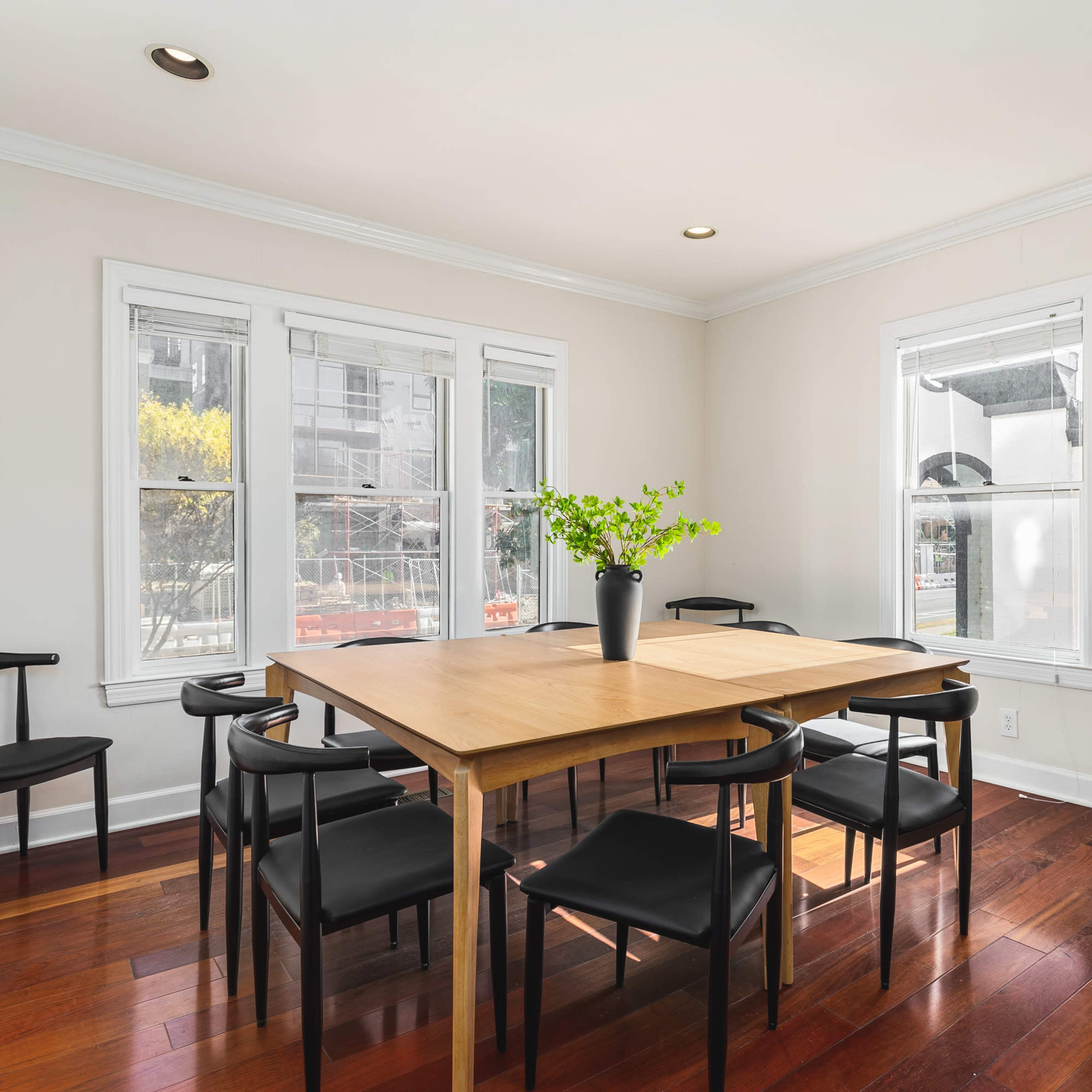 A dining area features a wooden table surrounded by black chairs and large windows allowing natural light.