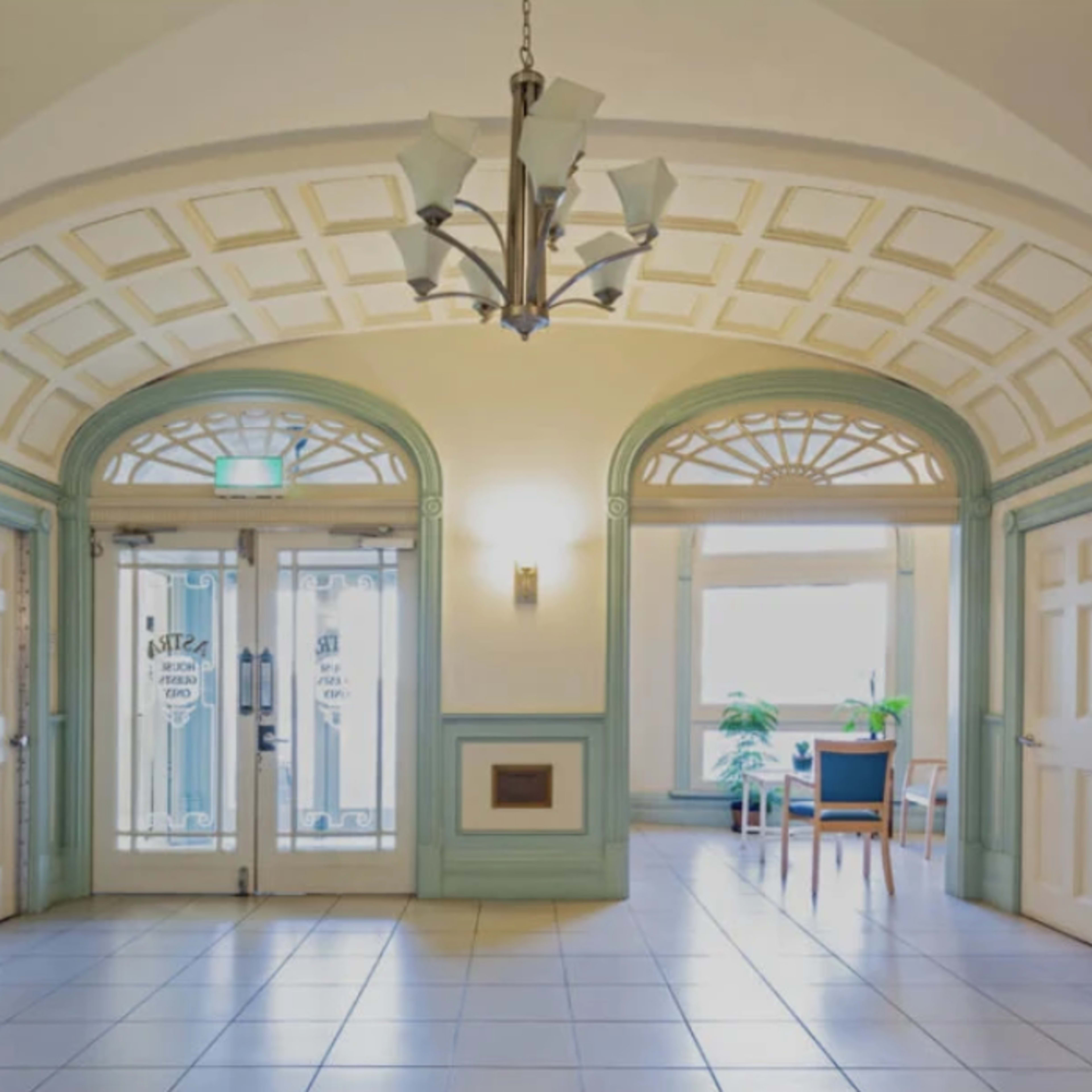 An elegant hallway with arched ceilings, two glass-paneled doors at the entrance, and a seating area beside a window.