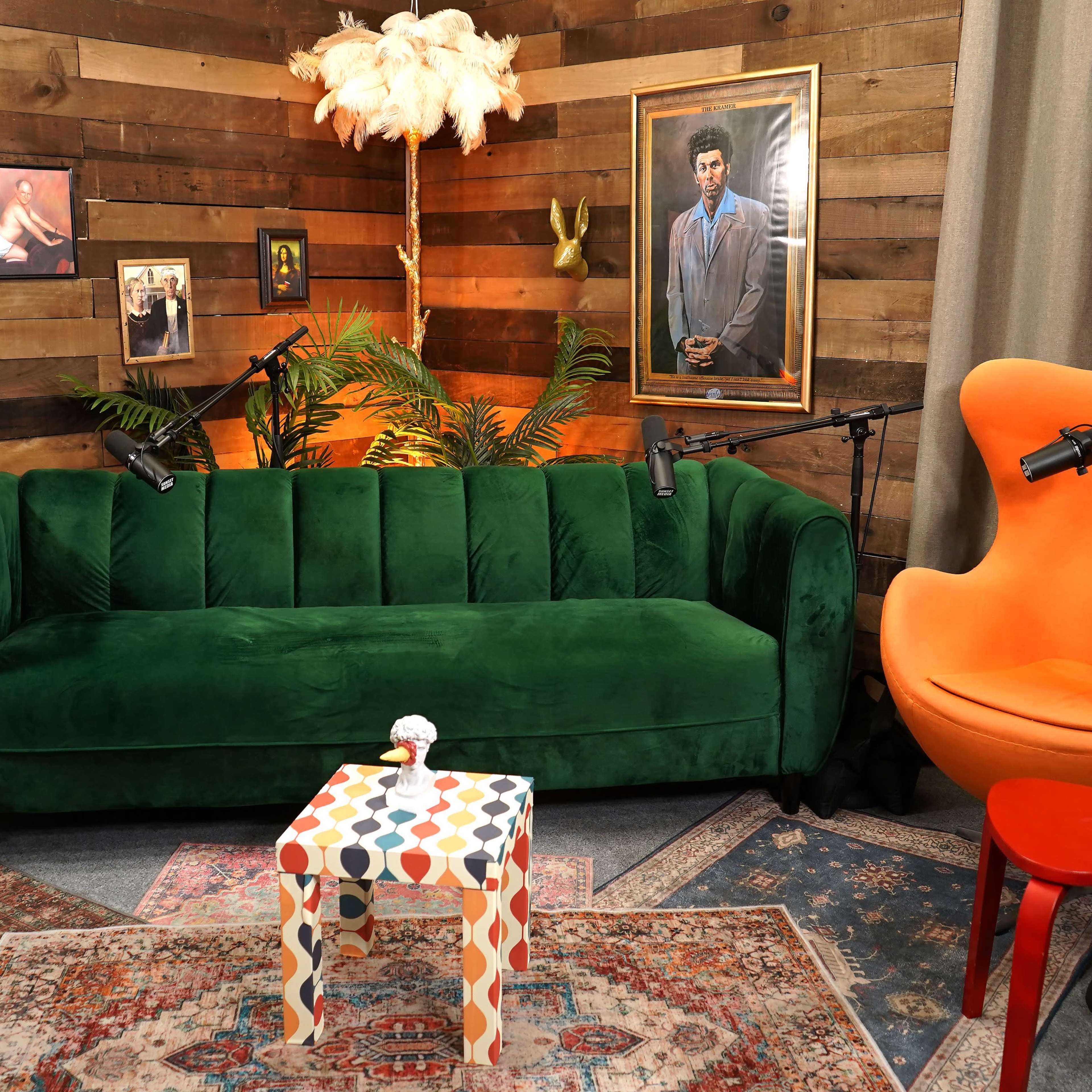 A cozy seating area with a green velvet sofa, an orange chair, colorful decor, and framed pictures on a wooden accent wall.