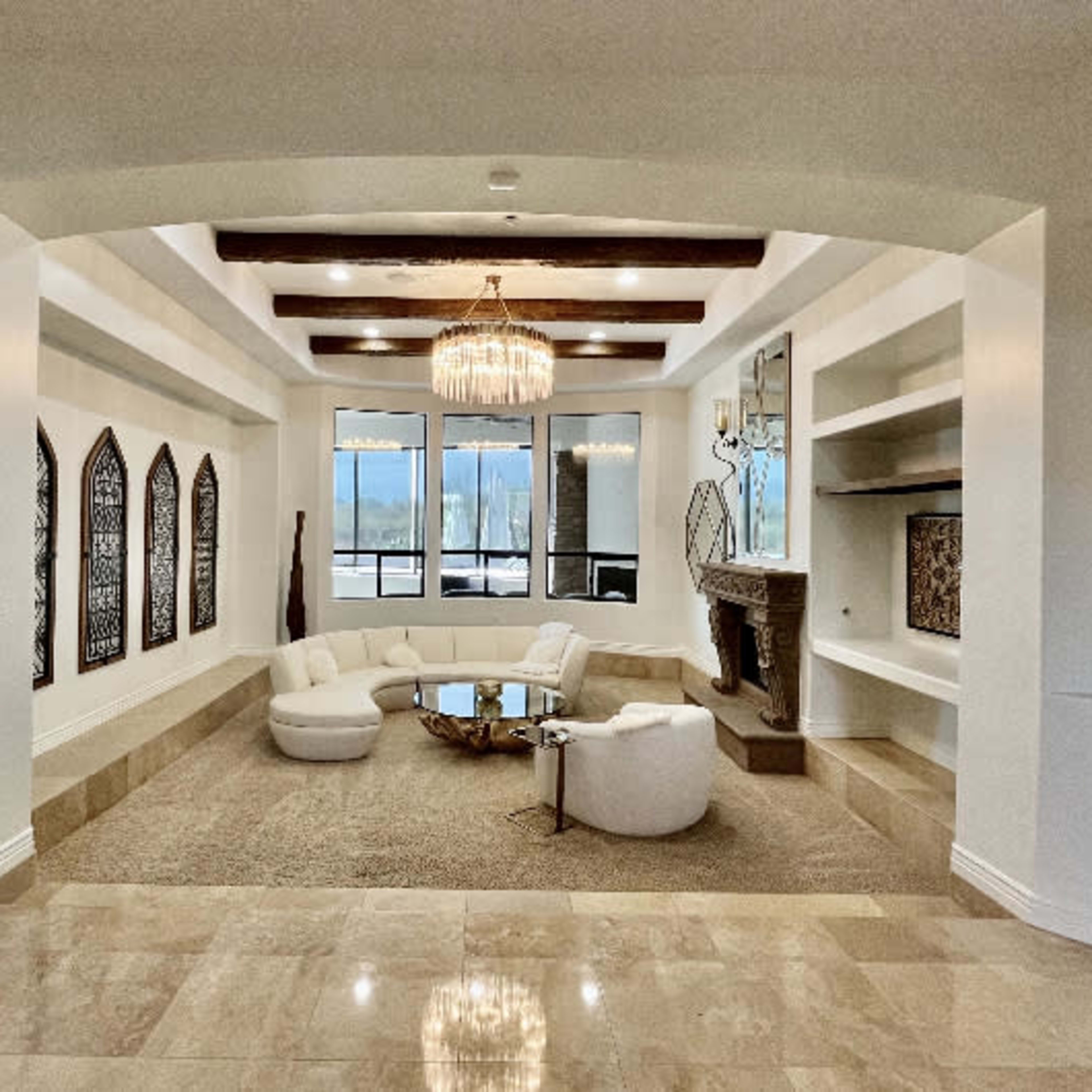 A spacious living room with a circular seating arrangement, a chandelier, large windows, and a stone fireplace.