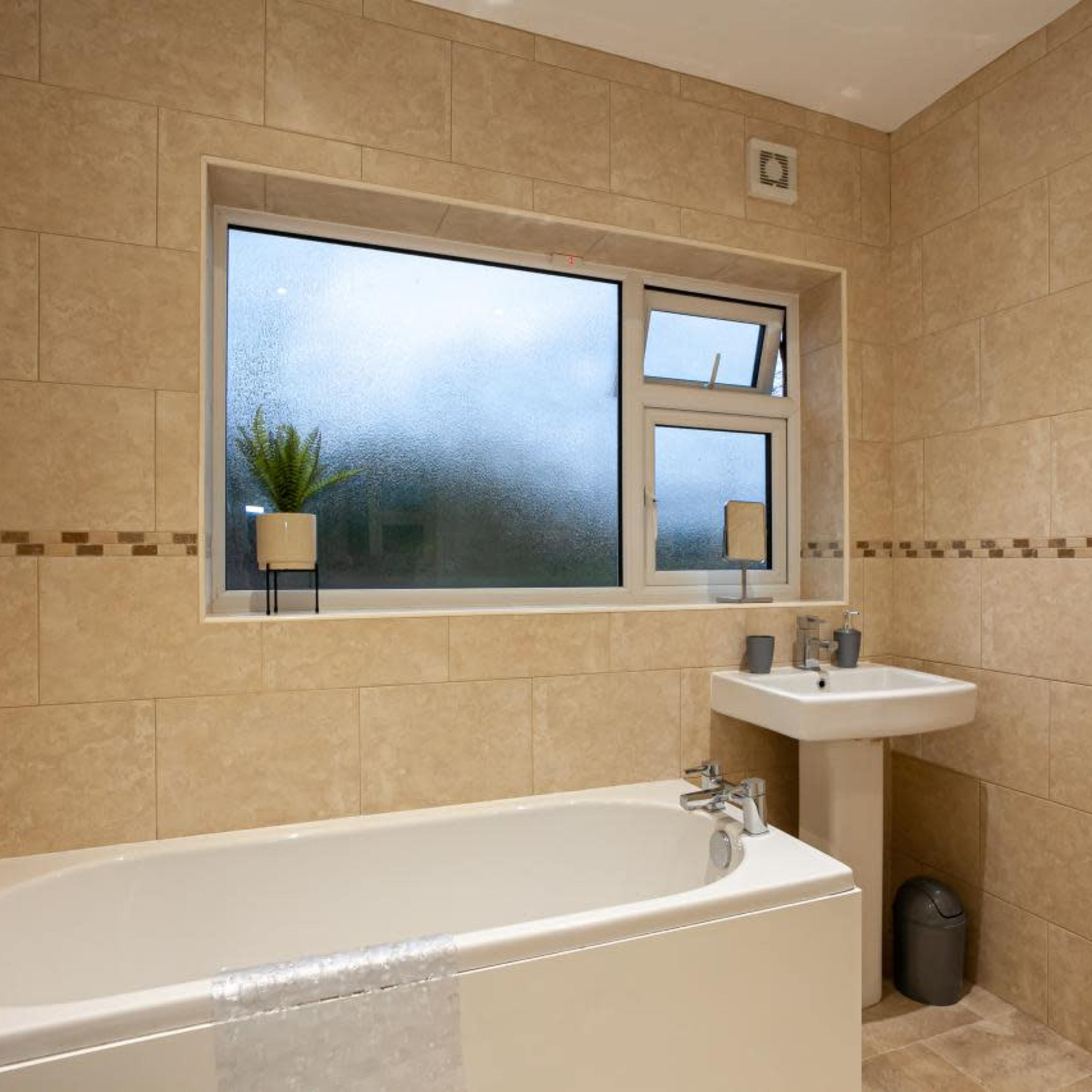 A bathroom features a bathtub, a sink, and a window partially obscured by condensation.