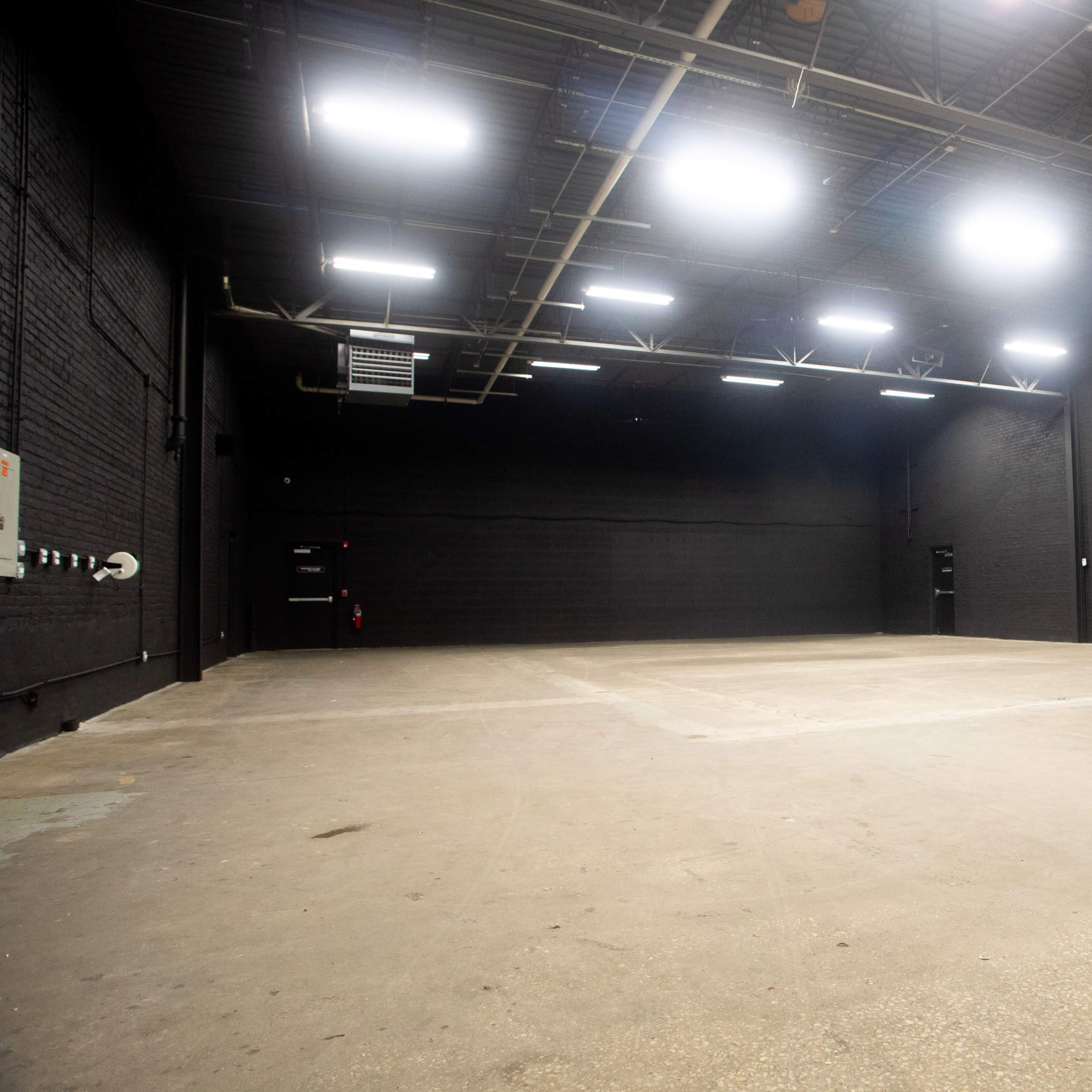 A large, empty industrial space with black walls and bright overhead lights.