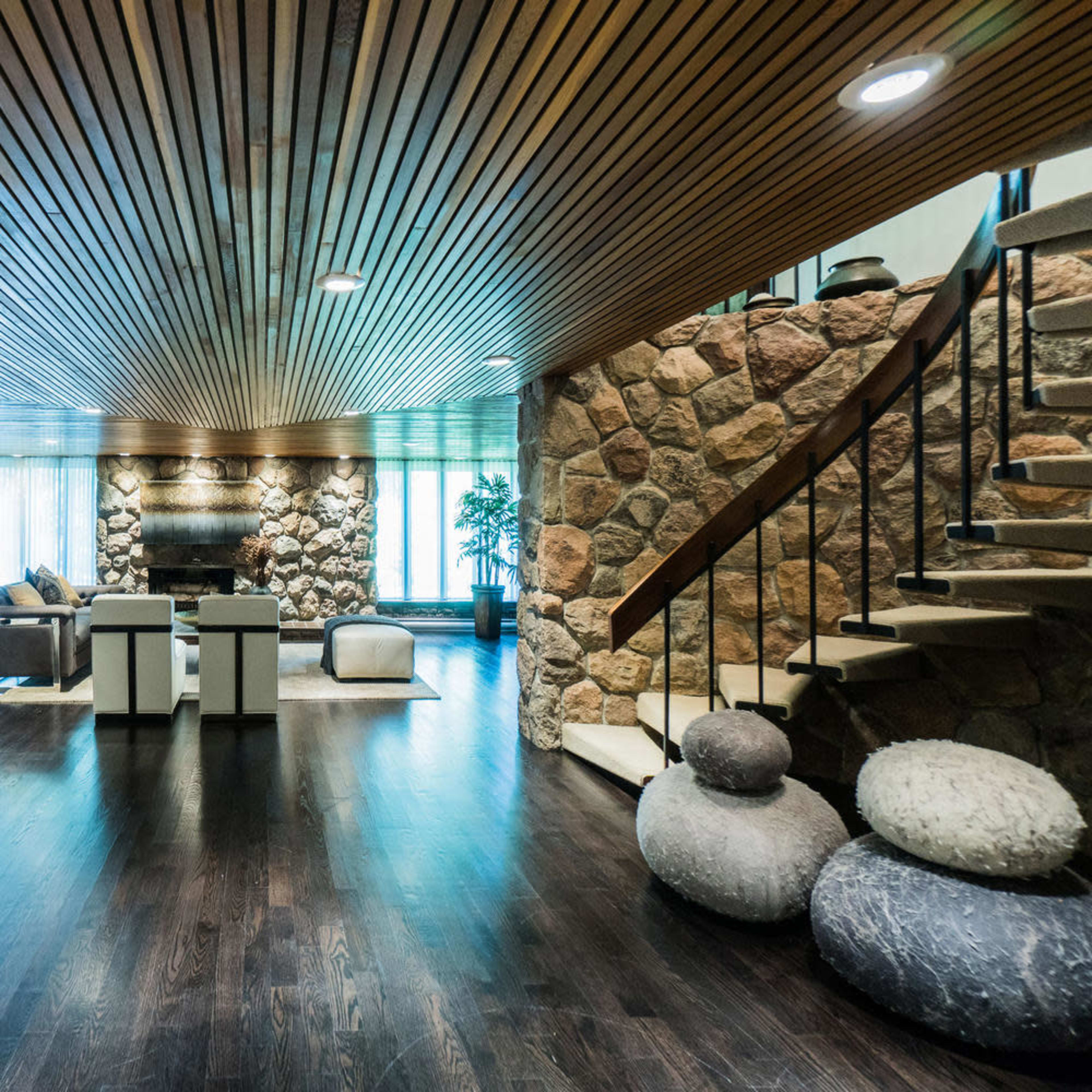 A spacious interior with a wooden ceiling, stone walls, and a staircase, featuring a seating area and a bar.