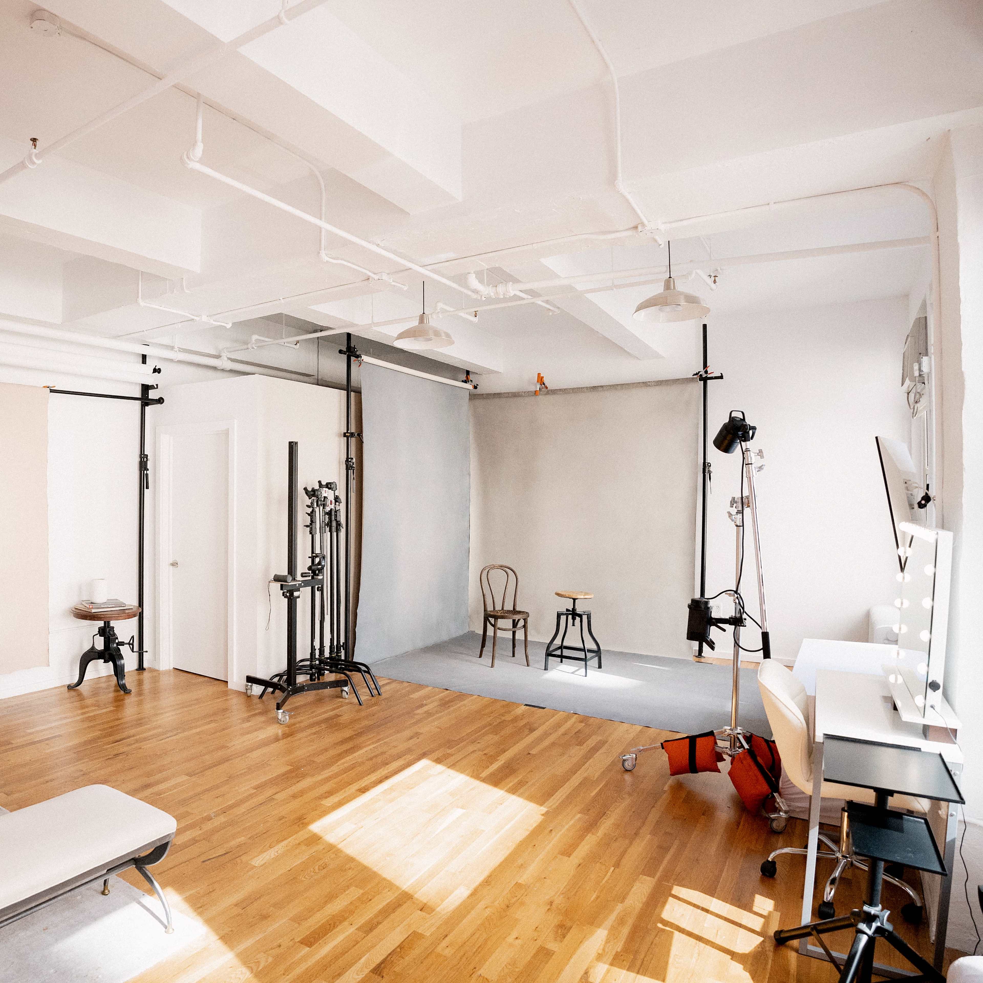 A spacious photography studio with wooden flooring, various backdrops, and lighting equipment.
