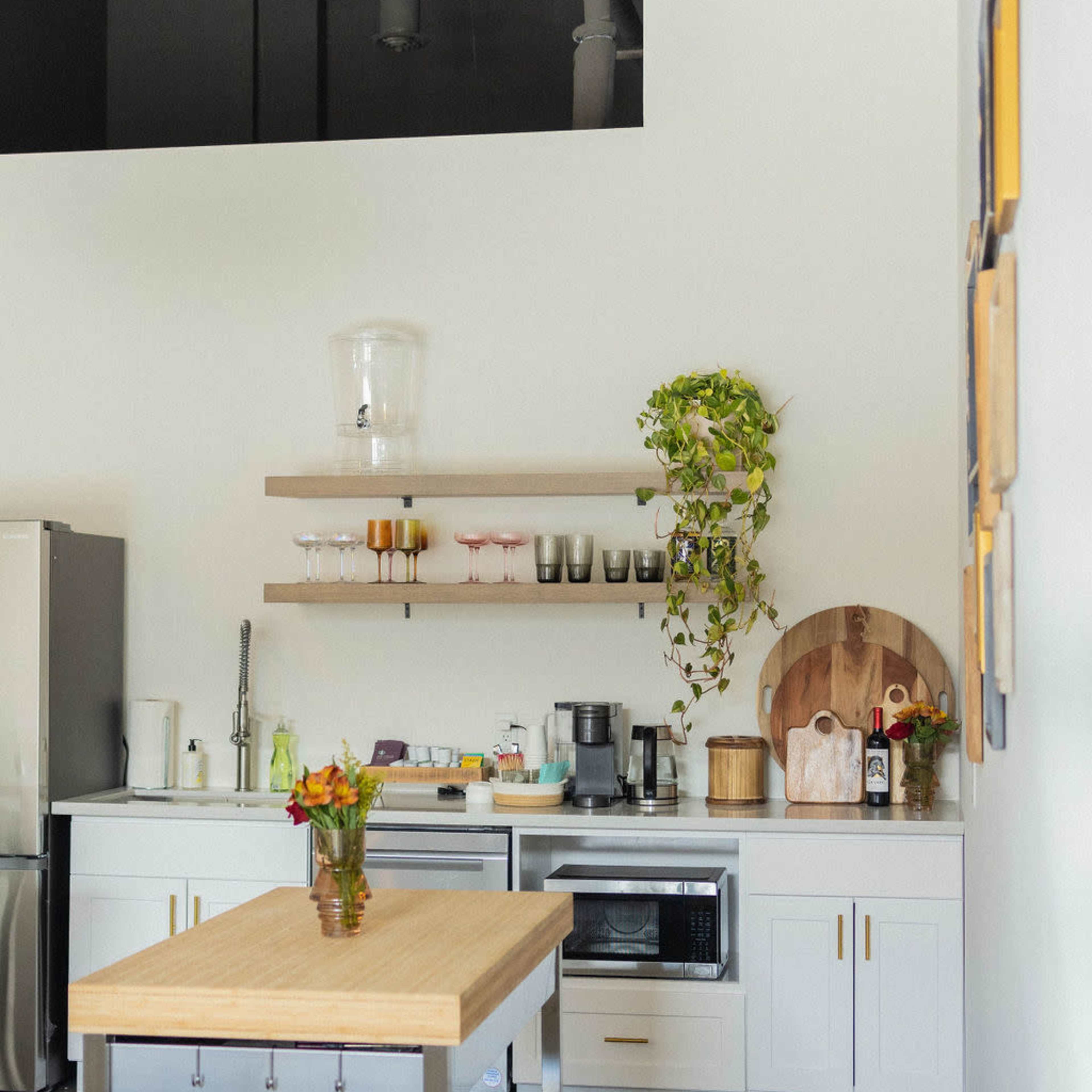 A modern kitchen with white cabinets, a wooden island, shelves with various kitchenware, and a potted plant.
