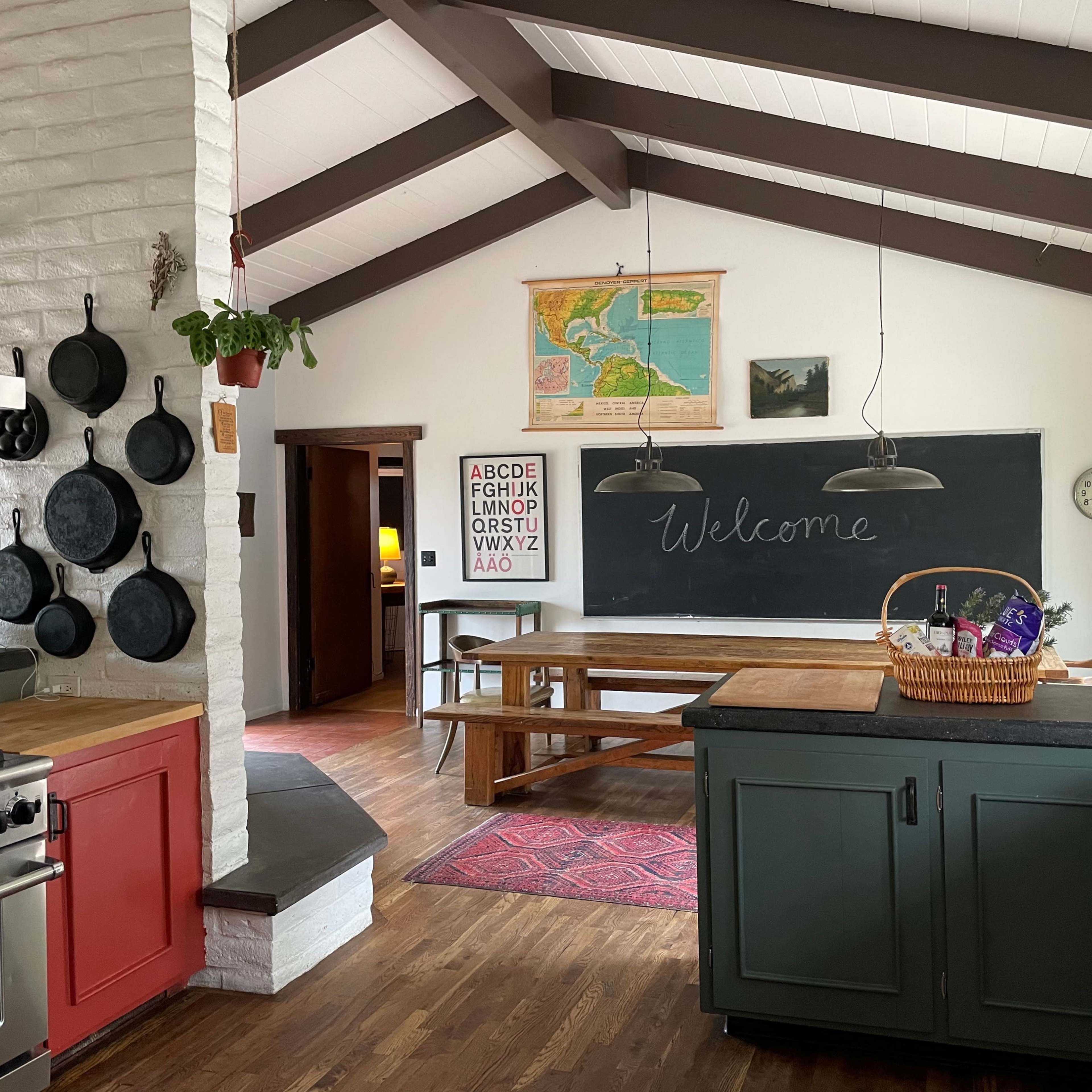 A spacious kitchen with a wooden dining table, chalkboard, wall-mounted pots, and an assortment of kitchen decor elements.