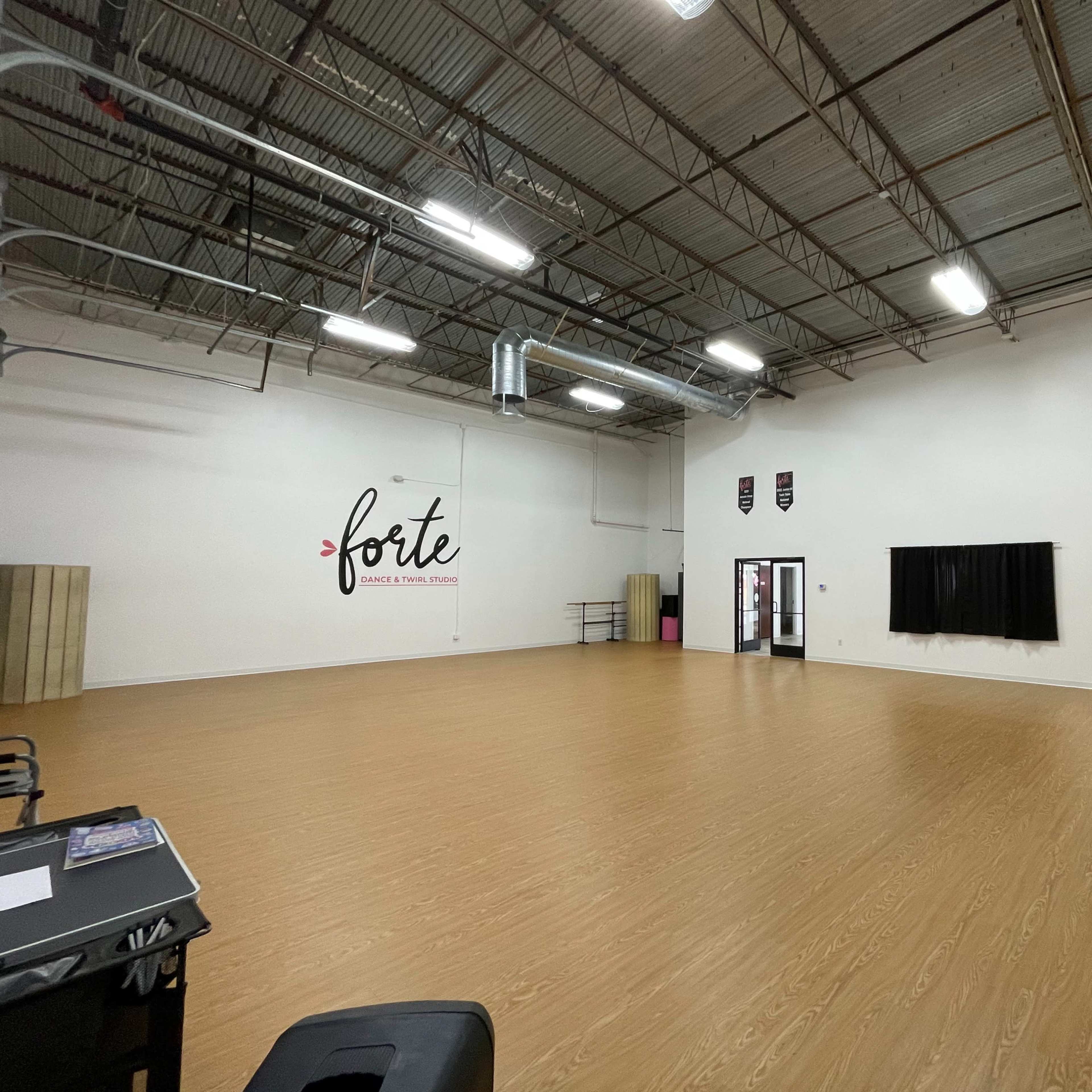 A spacious dance studio with a wooden floor, mirrors on one wall, and a large blank wall decorated with the word "forte."