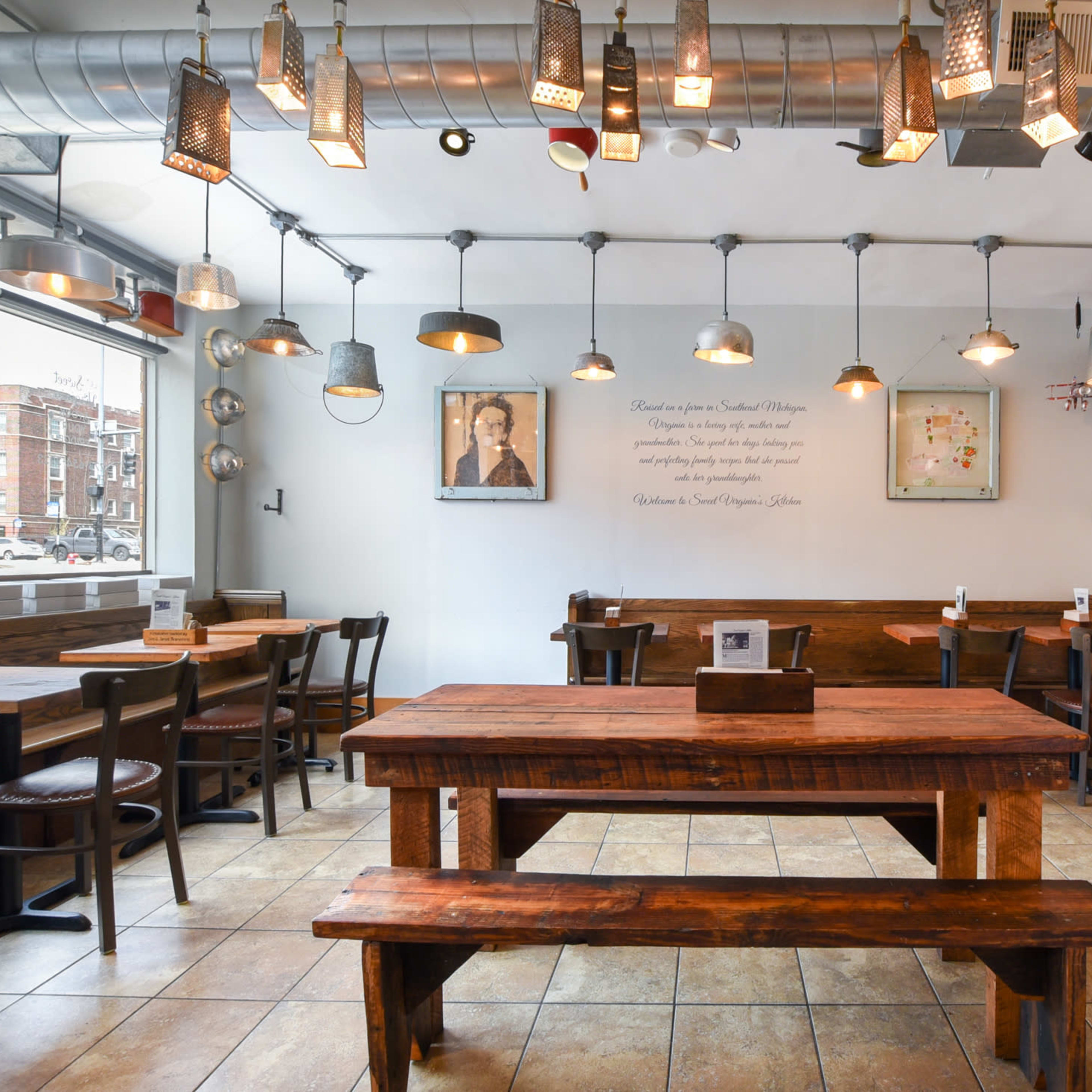 A rustic restaurant interior with wooden tables and benches, large windows, and industrial-style lighting.