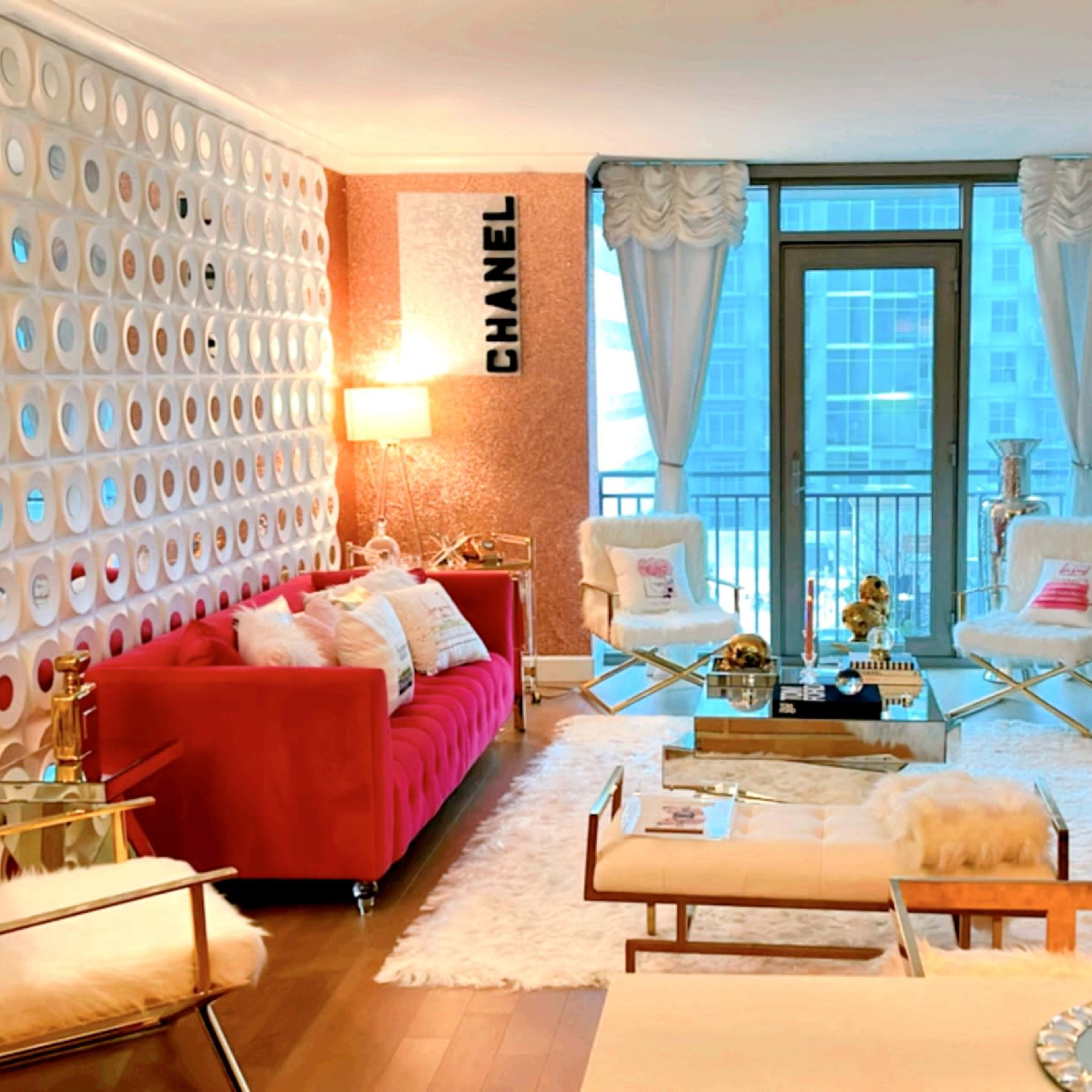 The living room features a red sofa against a decorative wall, a glass coffee table, and large windows overlooking a cityscape.