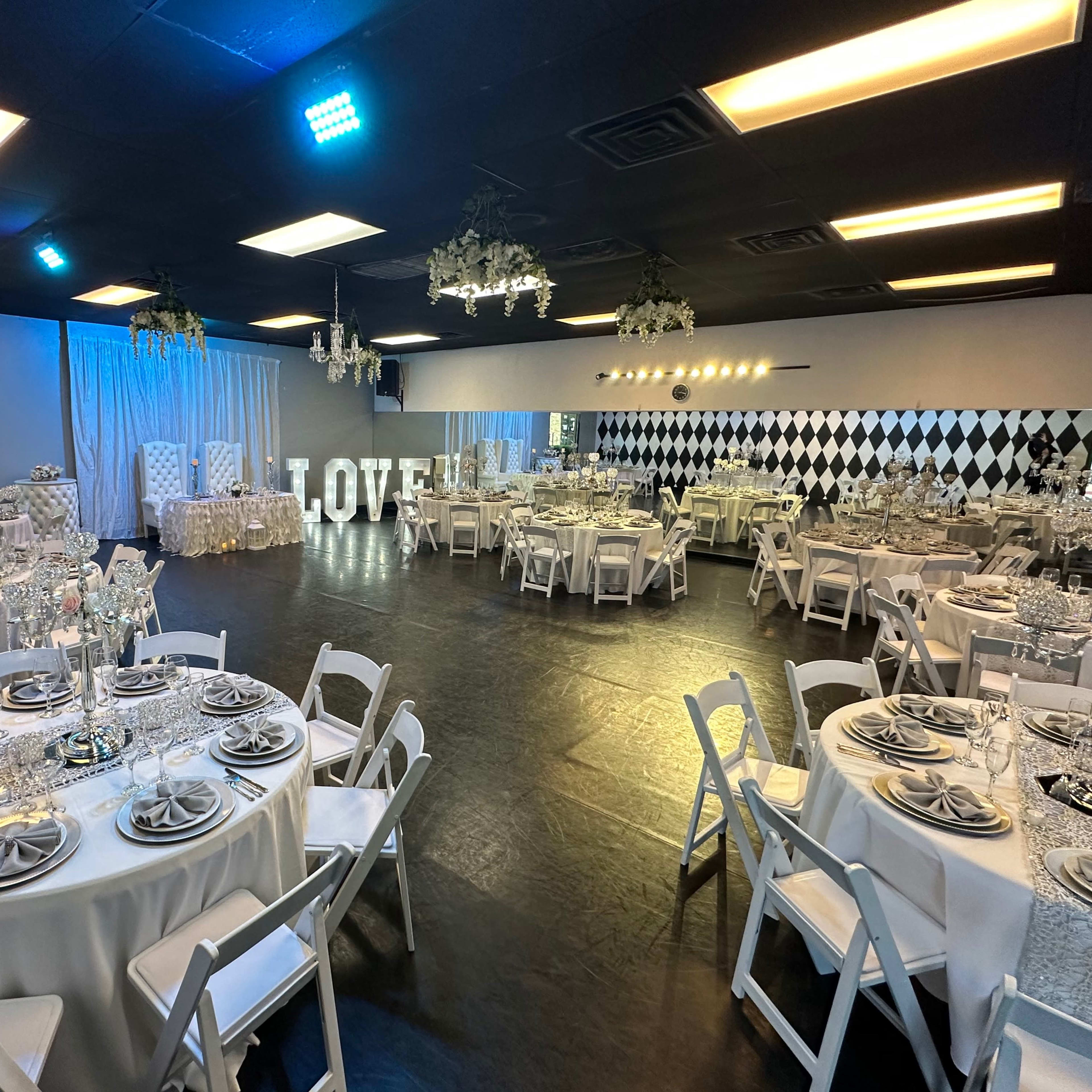 A decorated event space with round tables set for dining, white chairs, and a large 'LOVE' sign in the background amidst elegant decor.