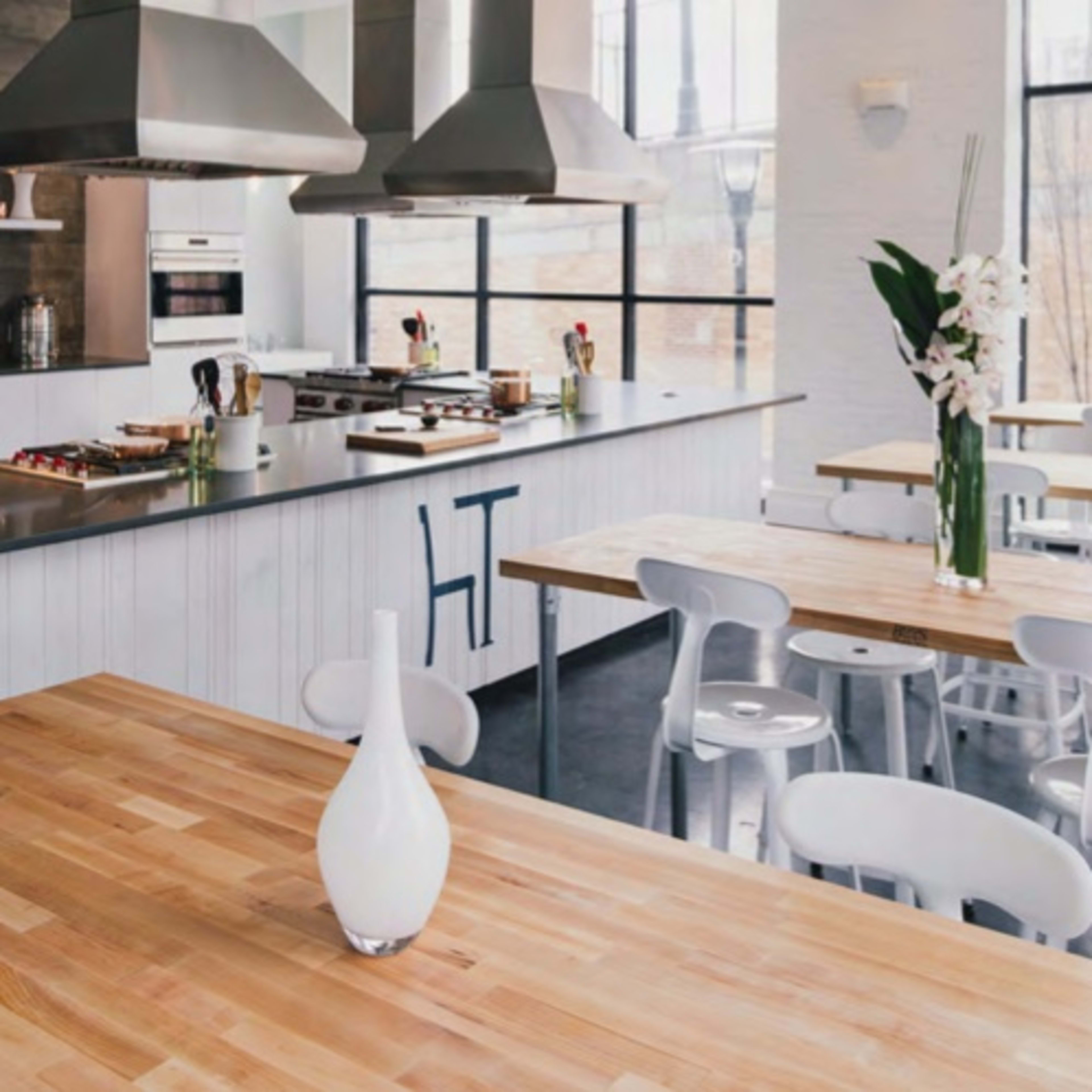 A modern kitchen features a large wooden table and a sleek cooking area with stainless steel appliances and large windows.