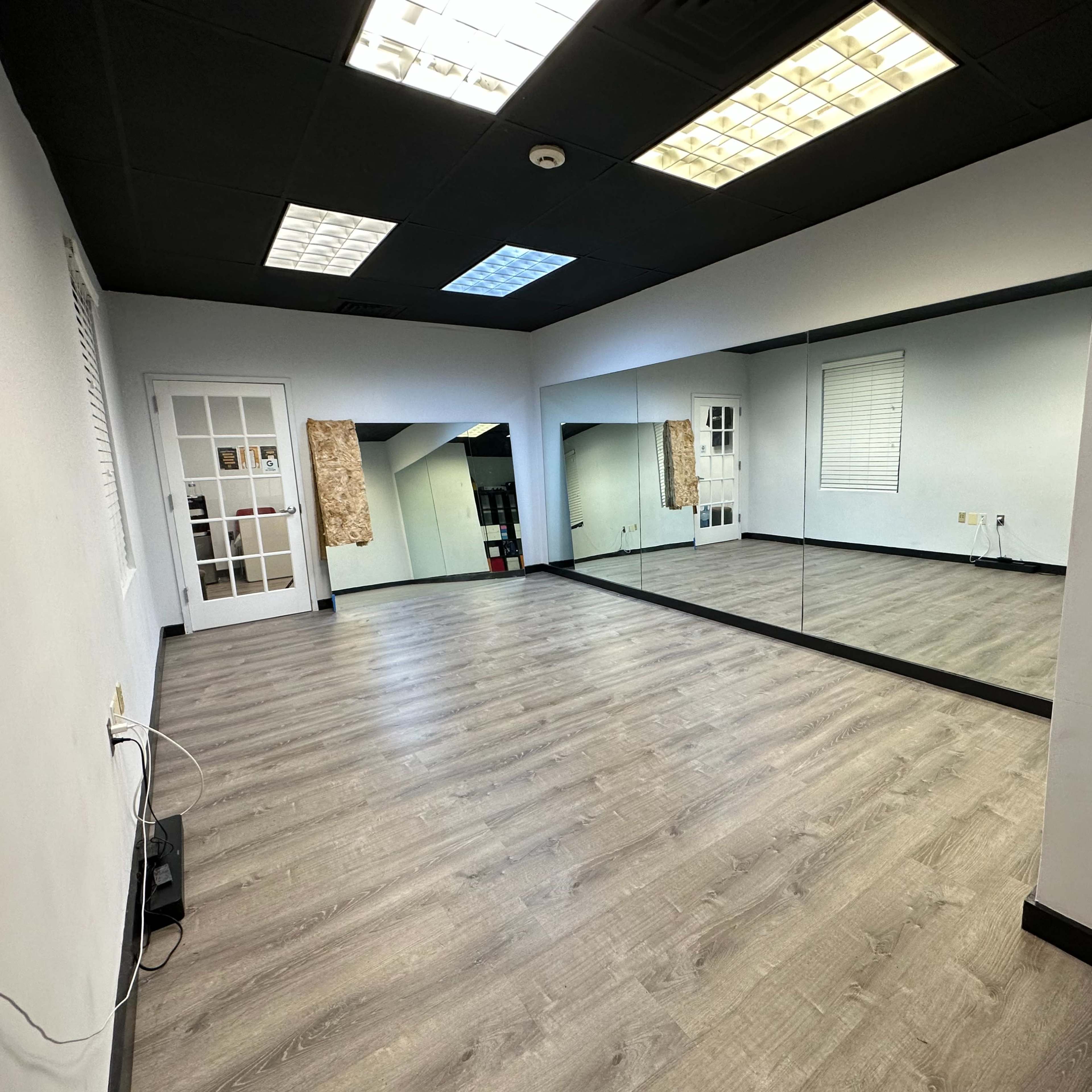 A spacious room with light-colored wooden flooring, a large mirror on one wall, and a door leading to another area.