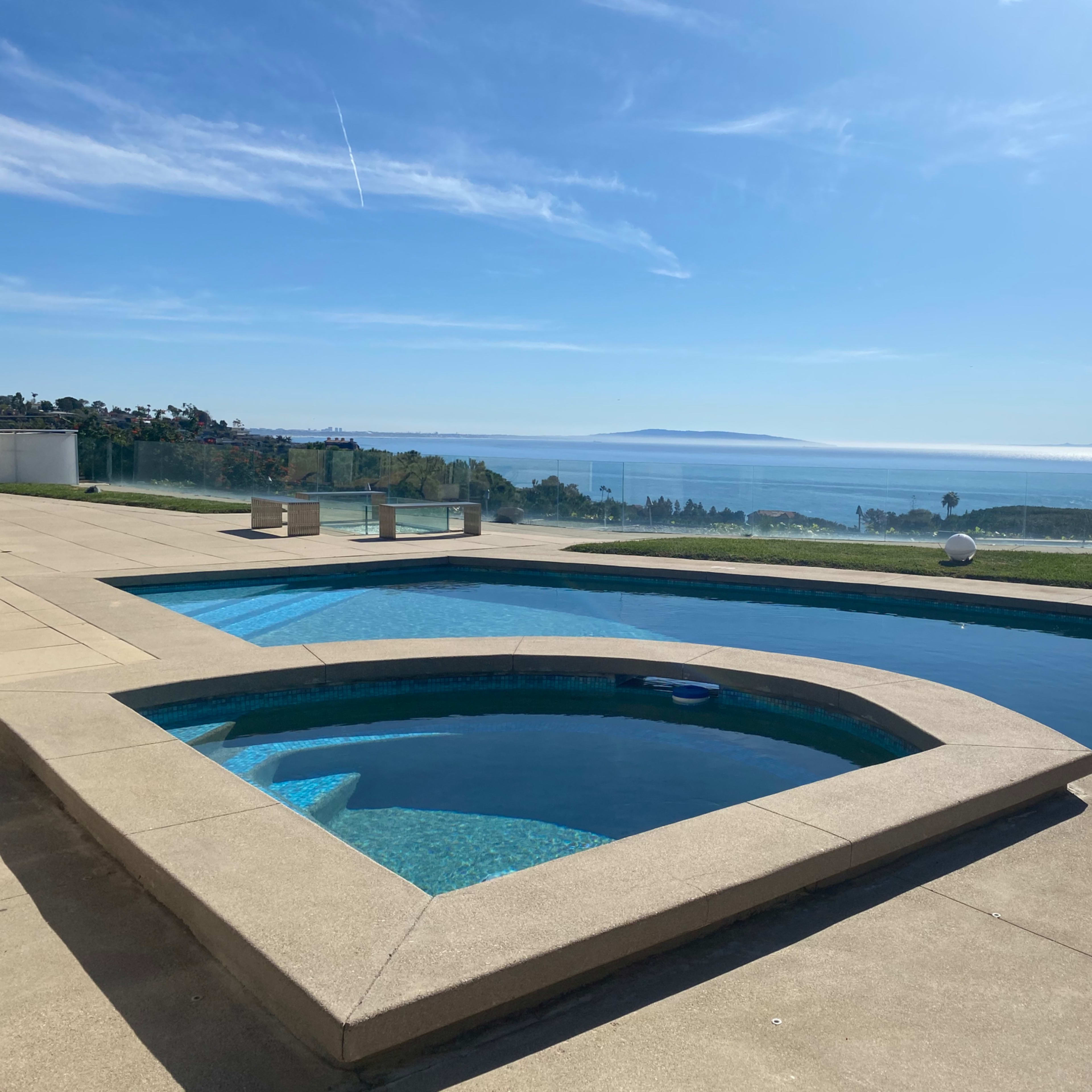 A pool area with a spa overlooking a vast ocean view under a clear blue sky.