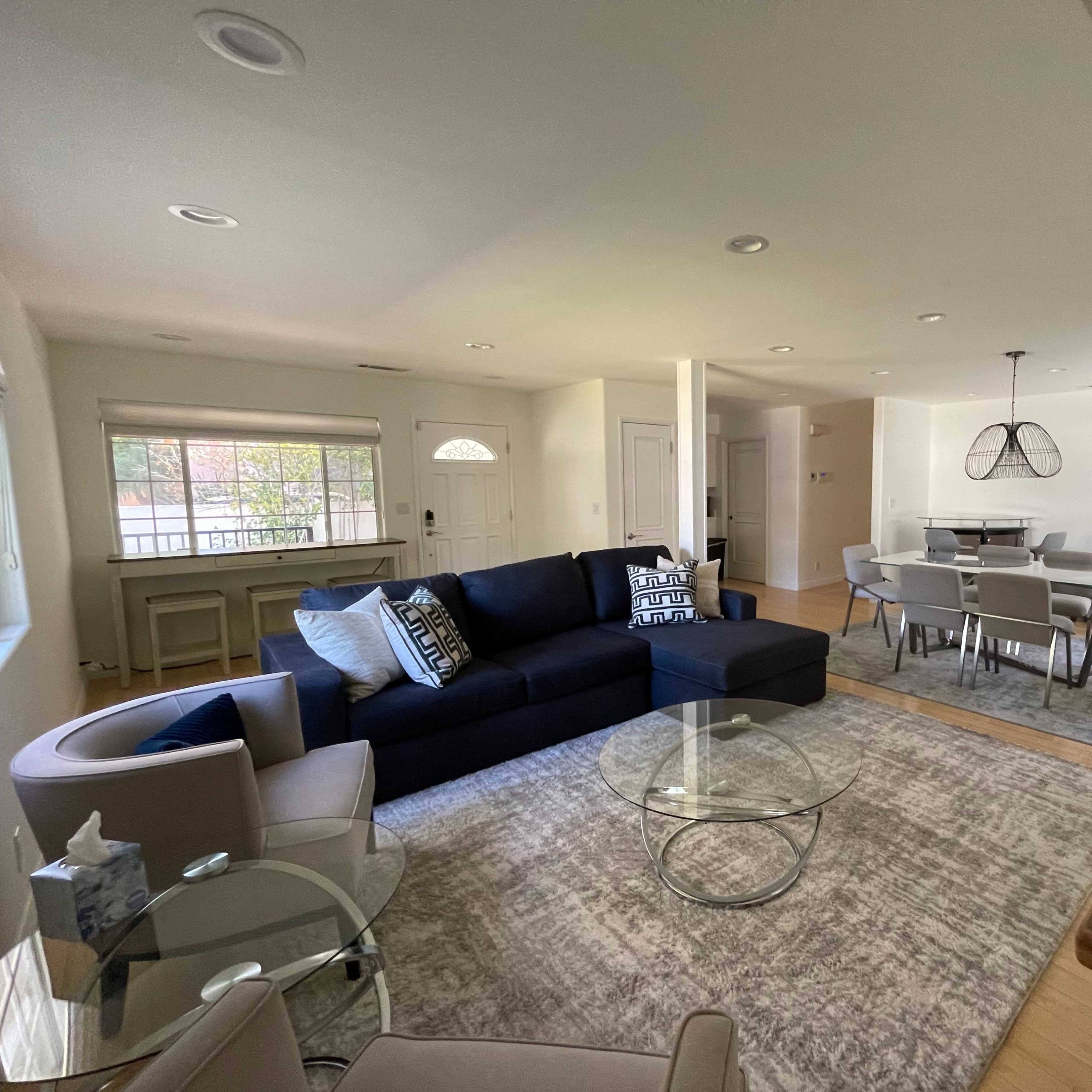 A modern living room with a sectional sofa, glass coffee table, and dining area featuring a rectangular table and chairs.