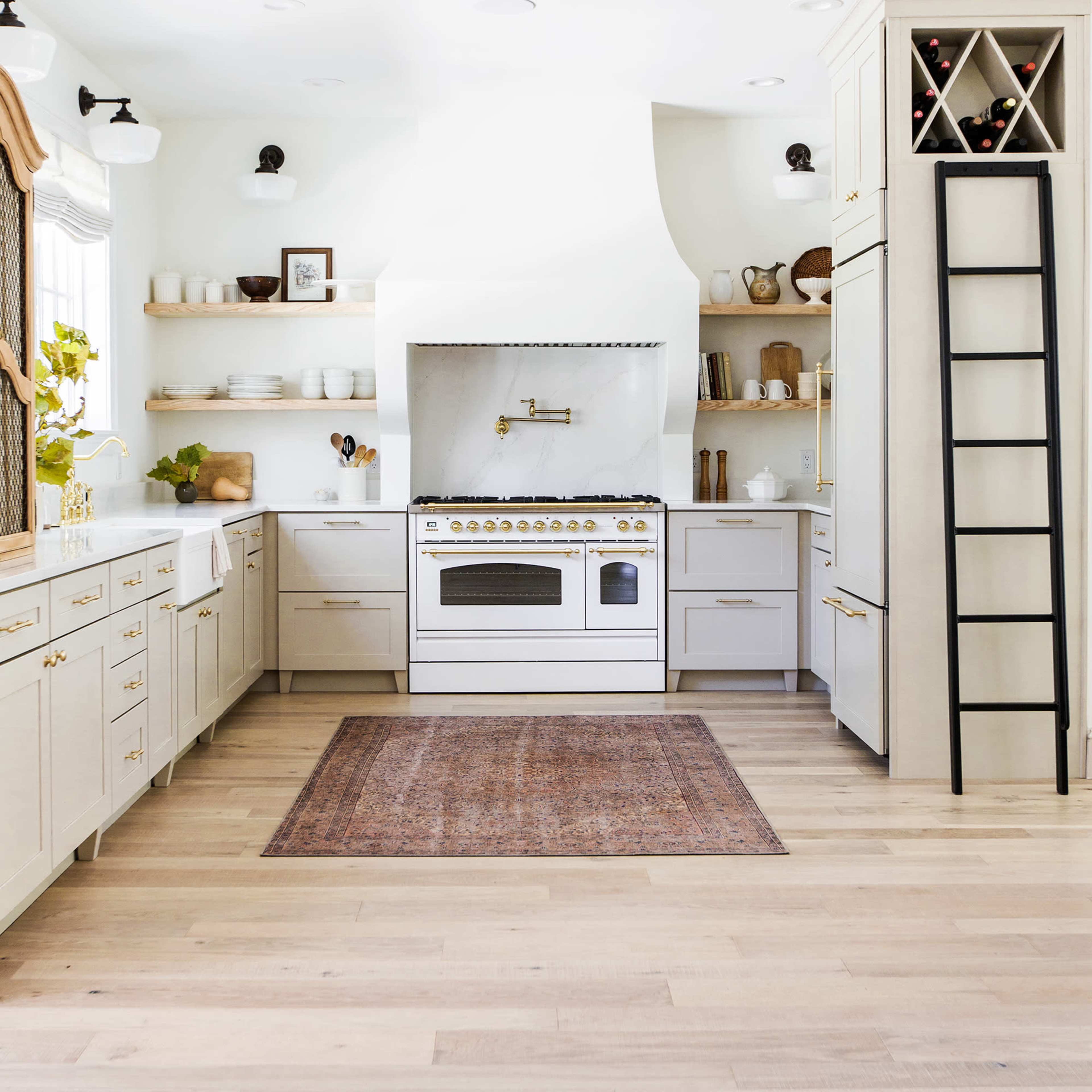 A sleek kitchen features a large stove centered under a hood, with light-colored cabinetry, open shelving, and a rug on the wooden floor.