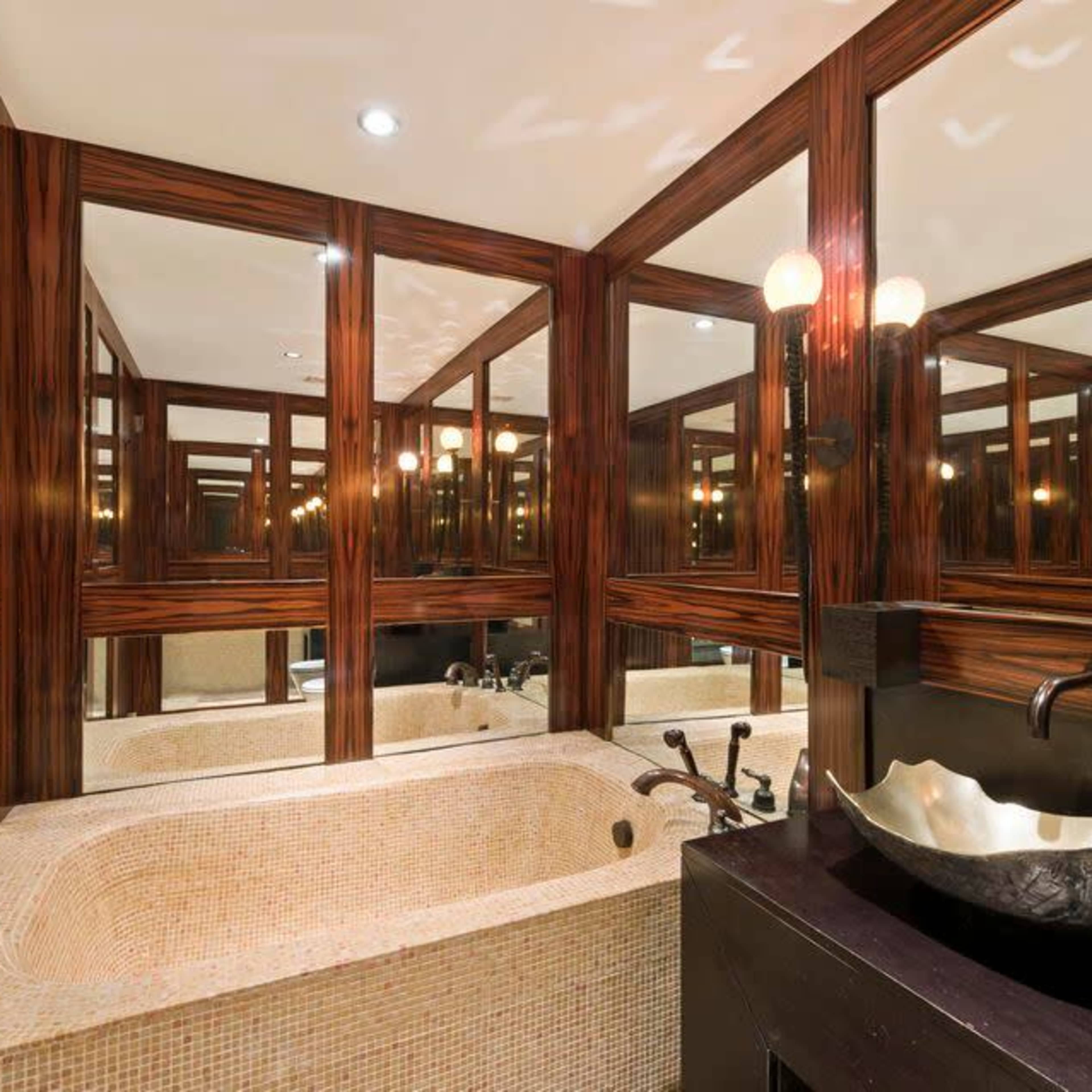 A modern bathroom with a large, sunken bathtub surrounded by mirrors and elegant wood paneling.