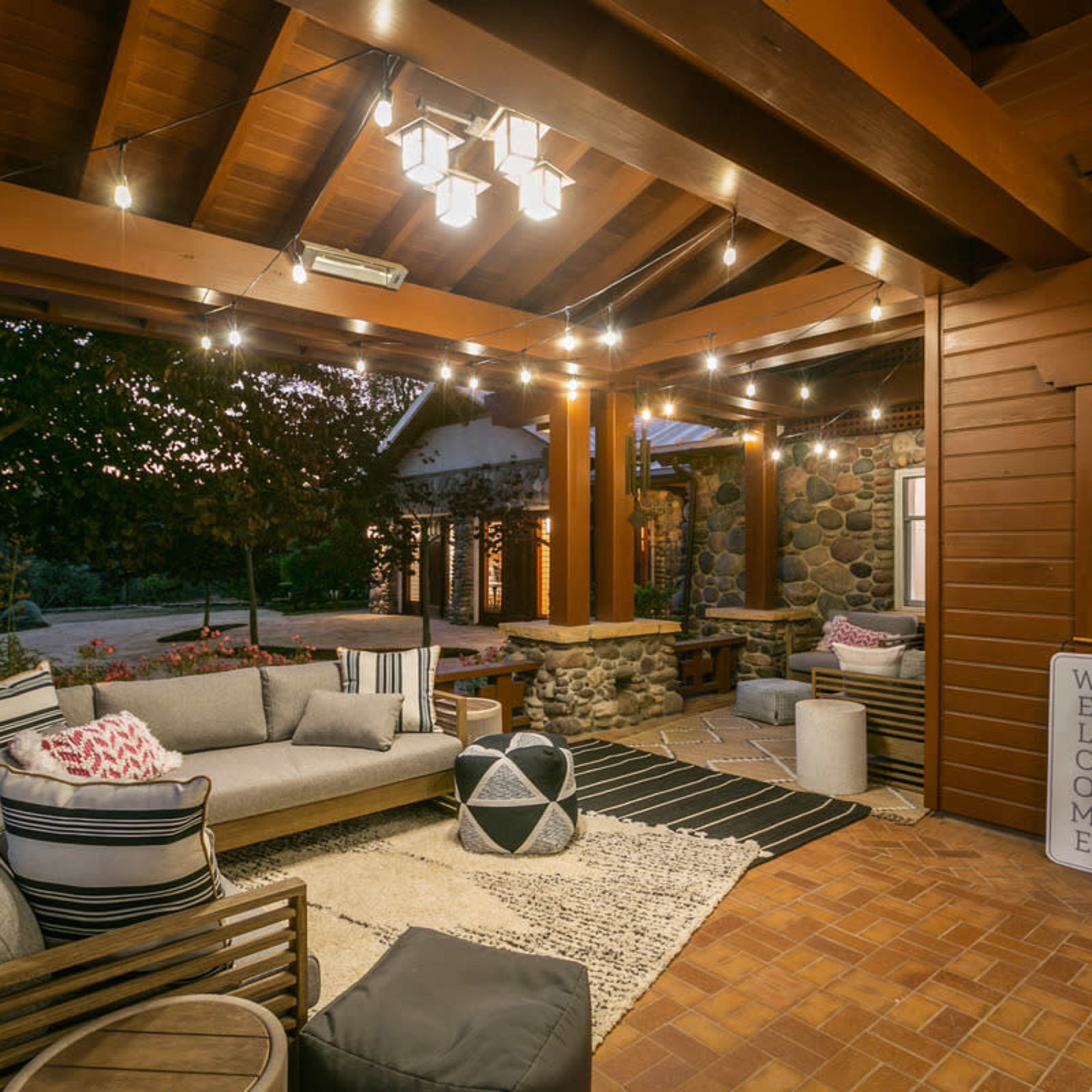 A cozy outdoor living space with a sectional sofa, patterned rug, and ambient string lights under a wooden pergola.