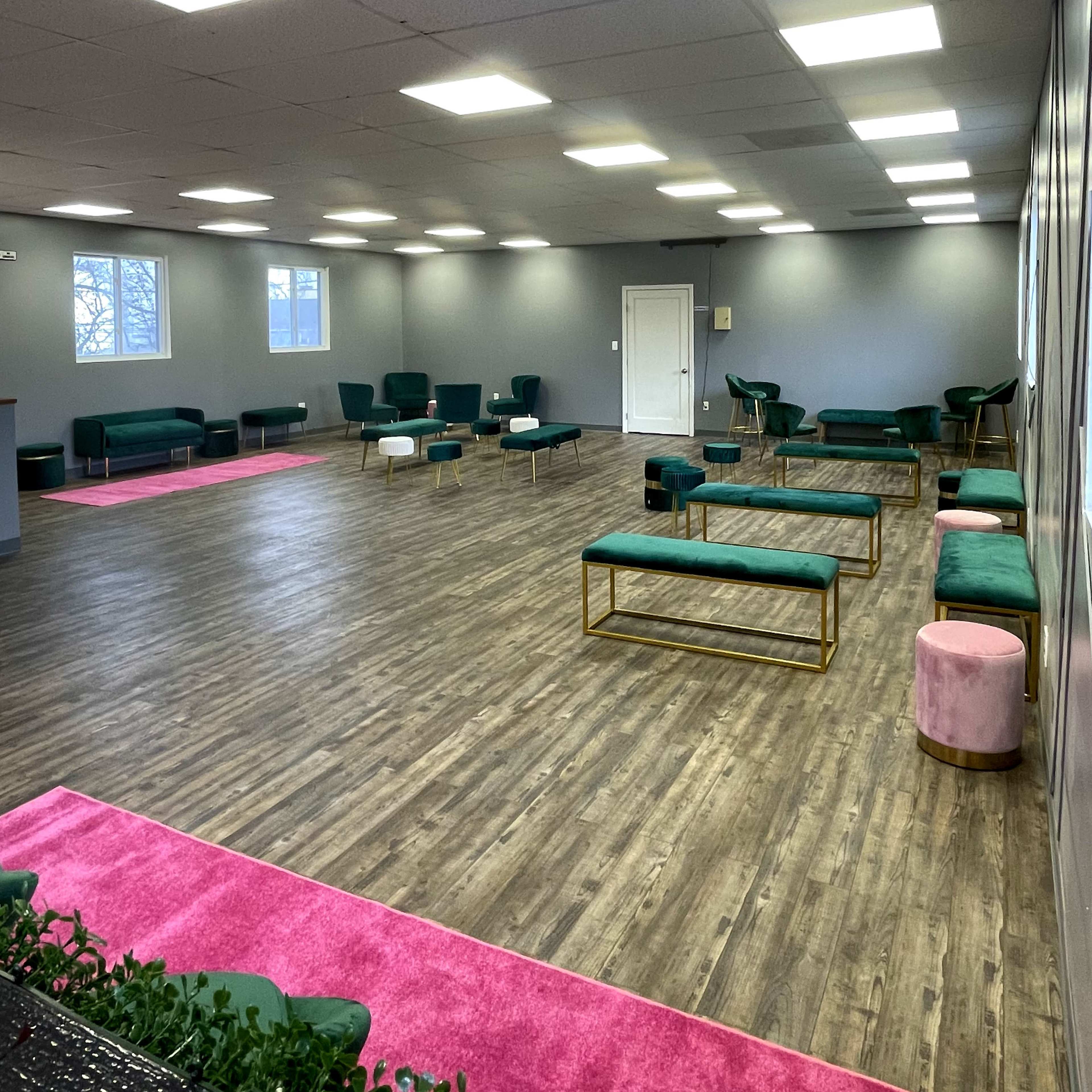 A spacious, well-lit room with wooden flooring, green seating areas, and pink carpets.