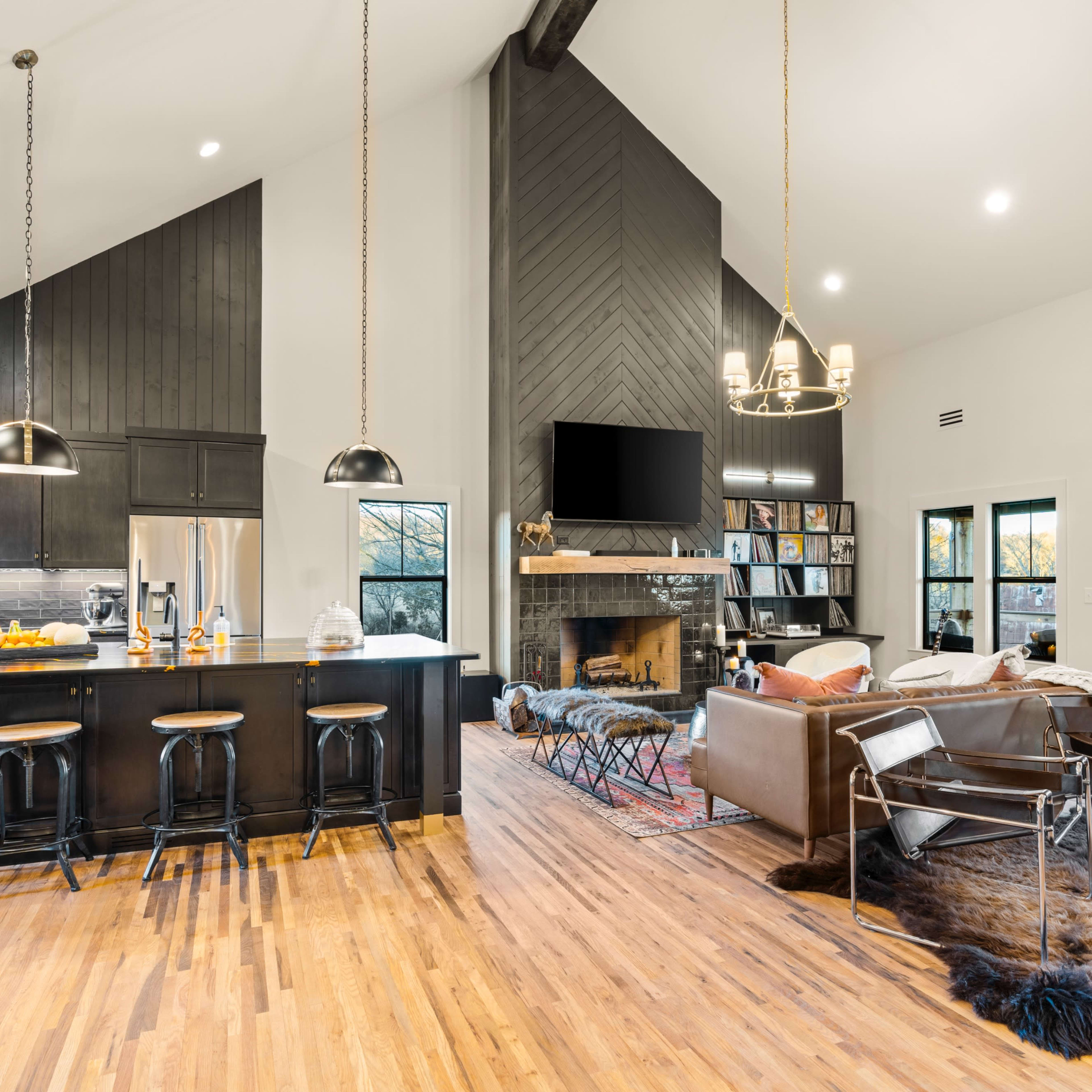 A modern open-concept living space with a kitchen, dining area, and living room, featuring high ceilings and a fireplace.