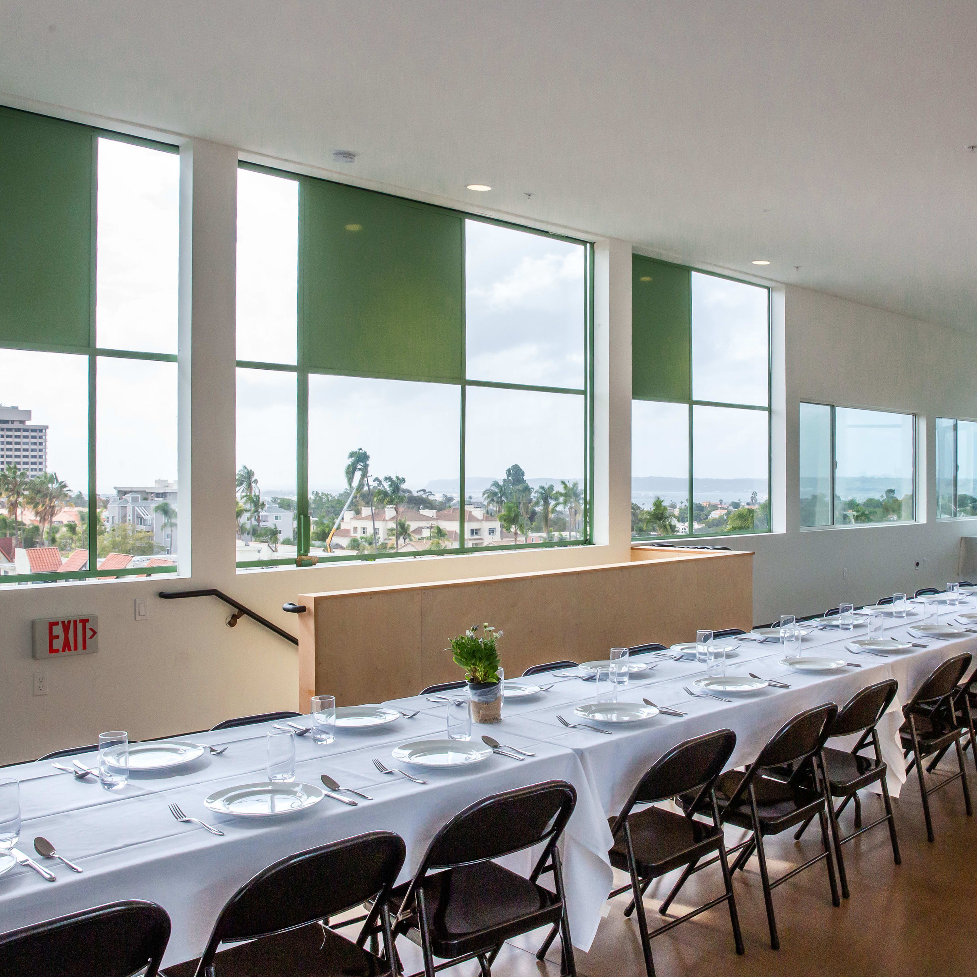 A long table set with plates and glasses is arranged by large windows overlooking a cityscape.