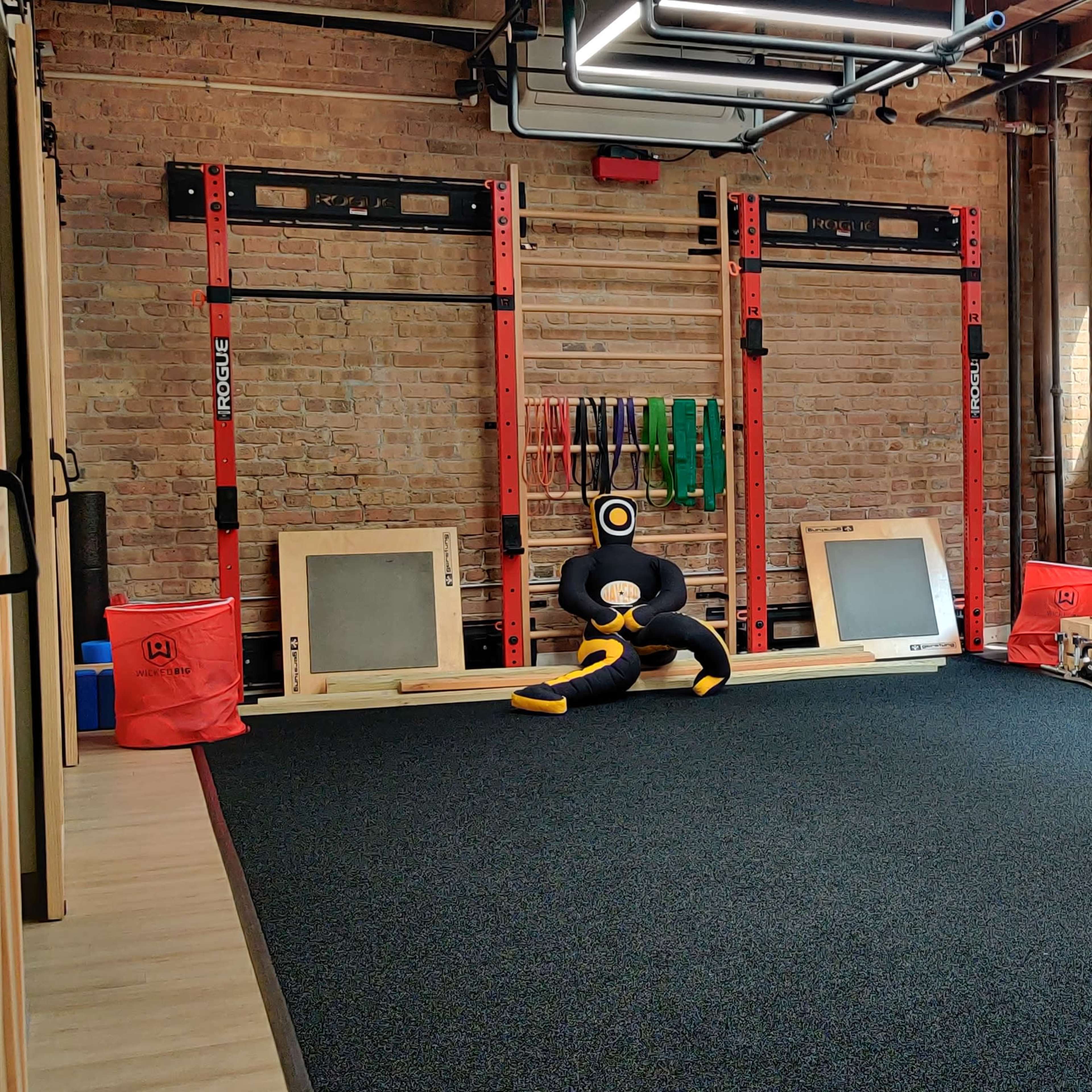 A fitness space features wall-mounted racks with exercise equipment, two wooden boxes, and a television, all set against brick walls and large windows.