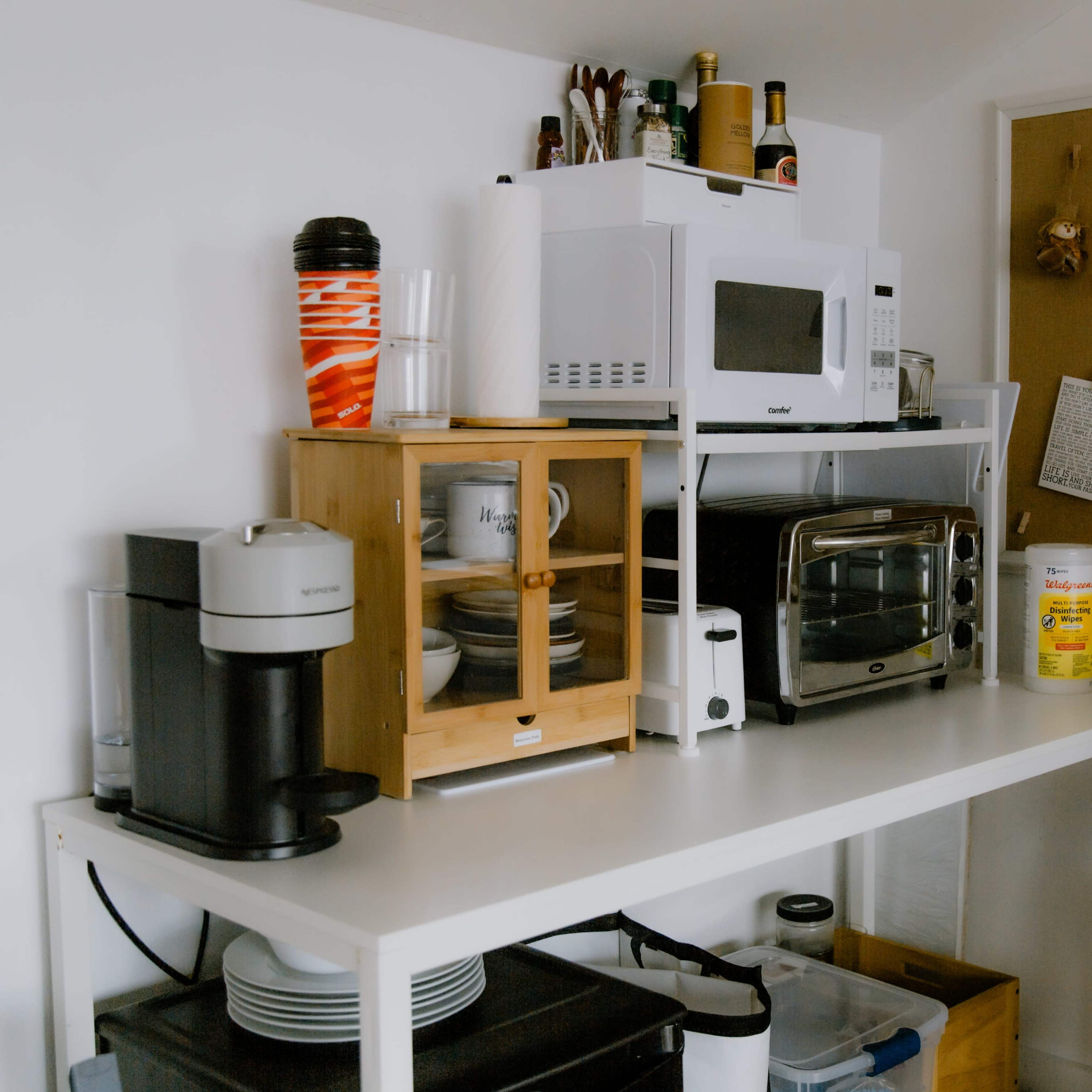 A compact kitchen area with a coffee maker, microwave, toaster oven, and organized shelves containing dishes and kitchen supplies.